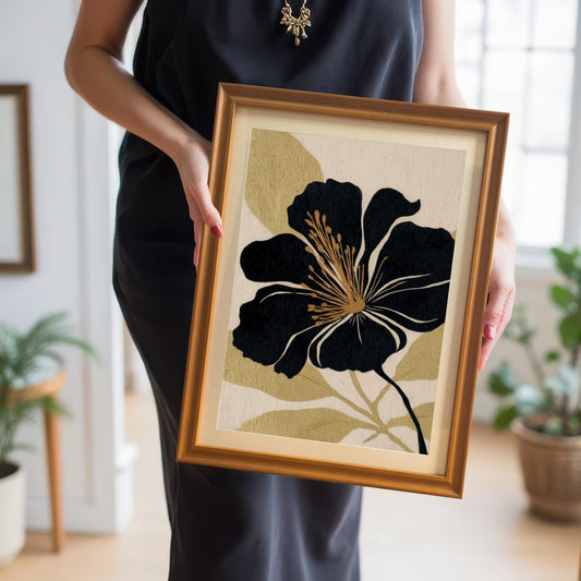 A person in a black dress holds the black and gold floral art print in a gold frame, showcasing the artwork's scale and frame color choice.