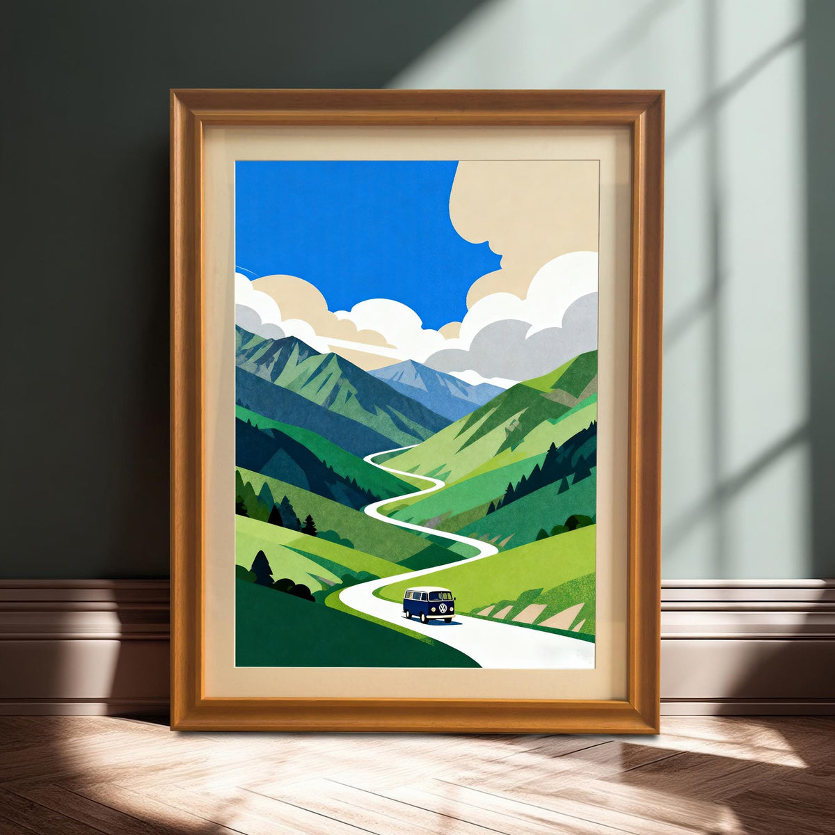 A large, framed print of the blue van on the winding mountain road, in a warm Orange/Gold Frame, resting on a wooden floor against a dark teal wall, bathed in natural window light.