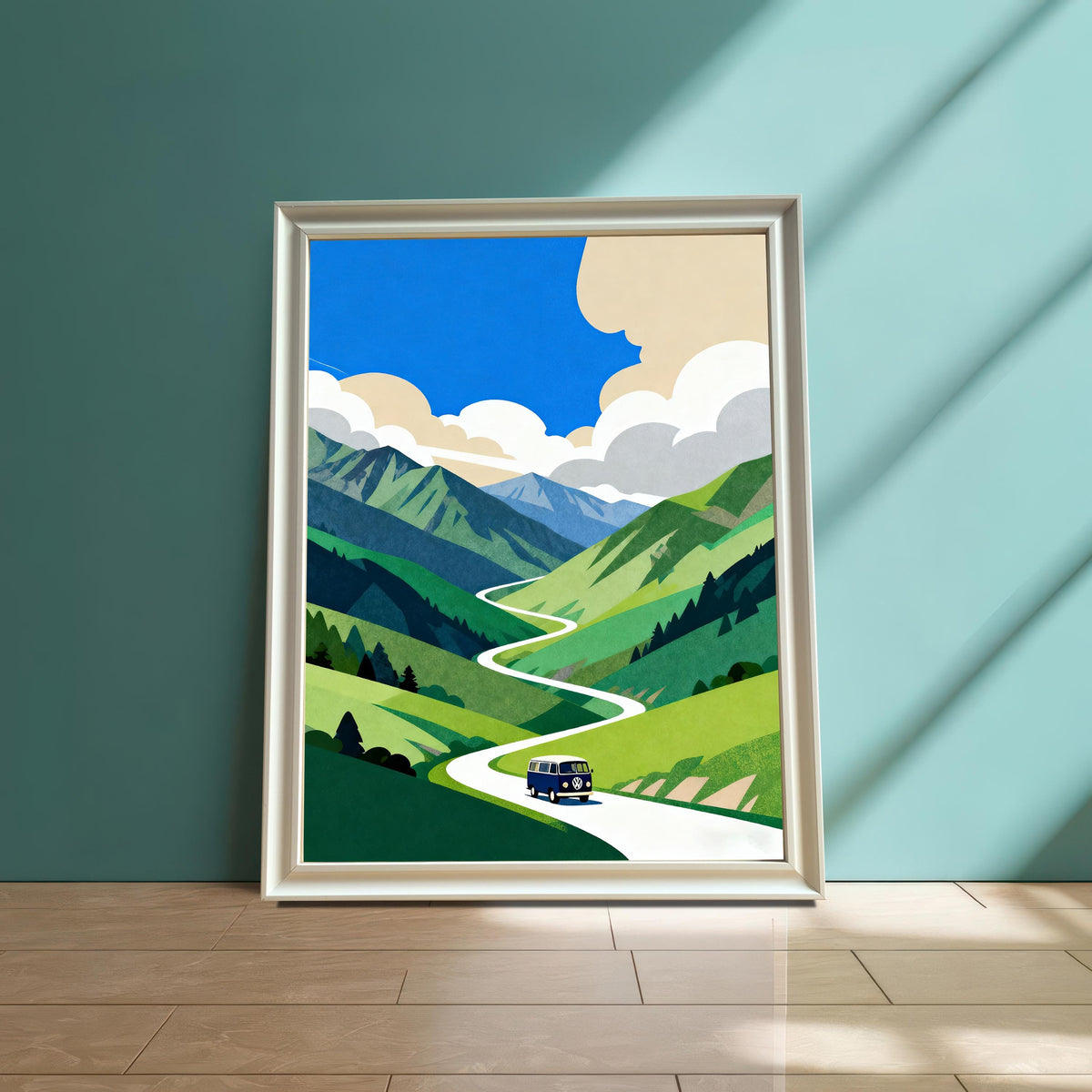 A framed print of a blue van on a winding road through green mountains, in a Silver or Light-Colored Frame, resting on a wooden floor against a dark teal wall.