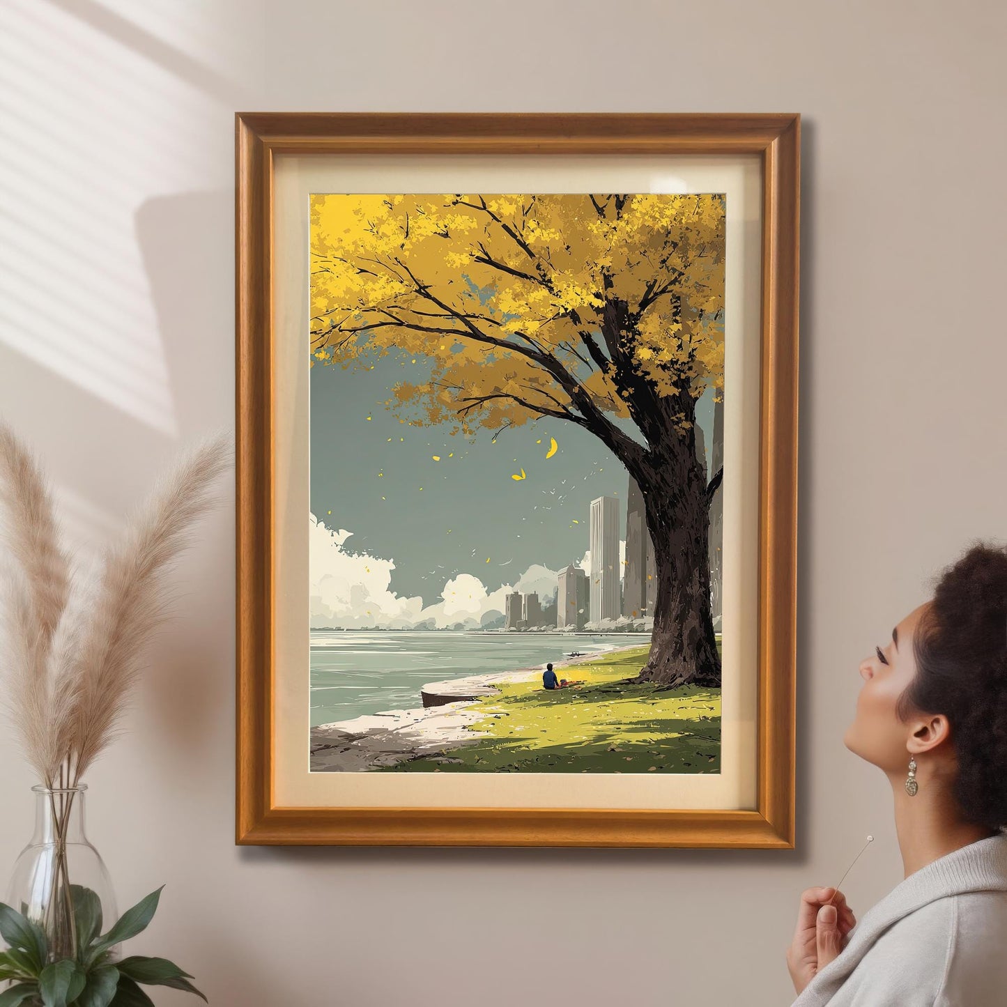 A woman admires the yellow autumn tree and city park art print which is framed in a gold/orange frame with a mount and hanging on a beige wall.