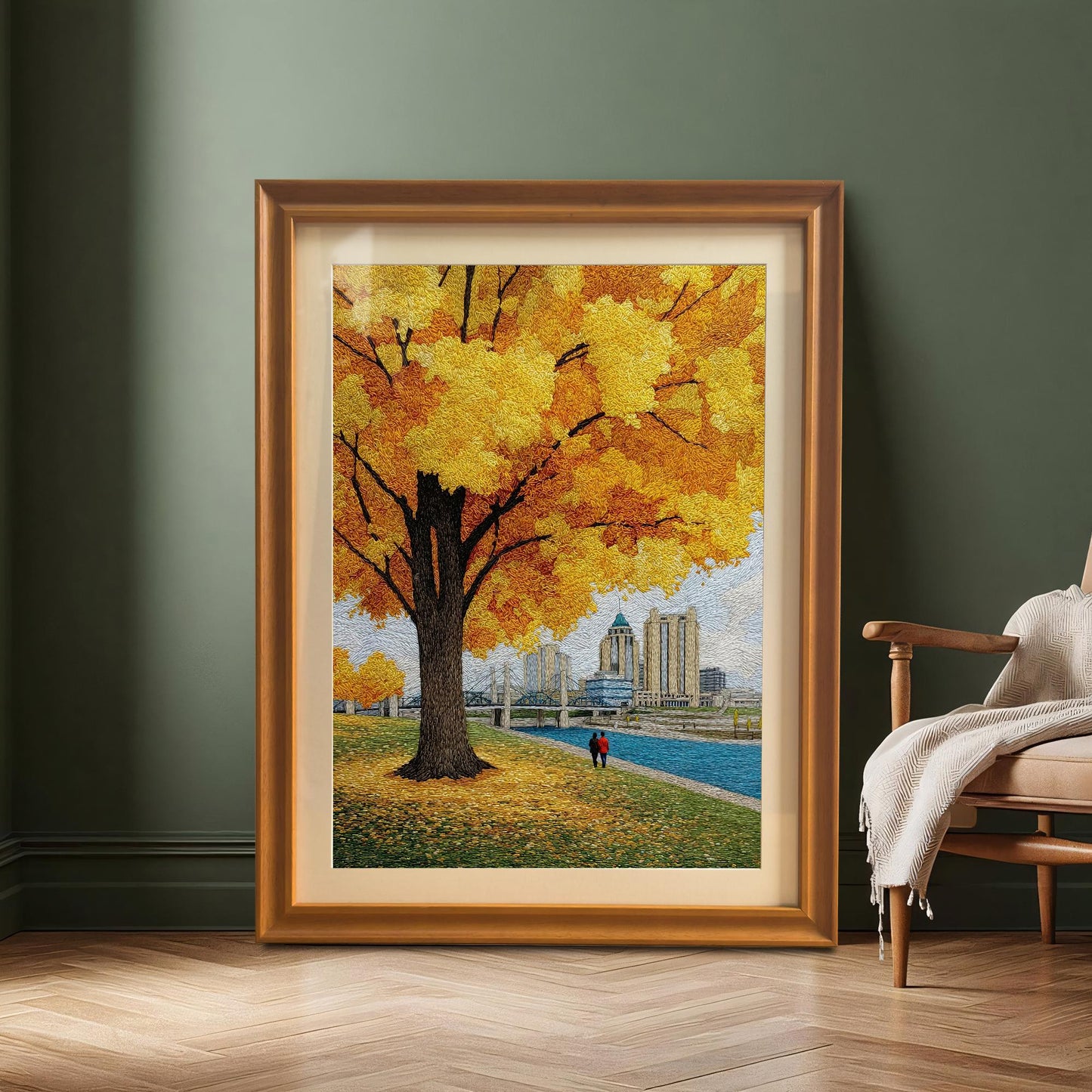 Large, full view of the textured yellow autumn tree and cityscape art print in a gold/orange frame with a mount leaning against a dark green wall next to a wooden chair.