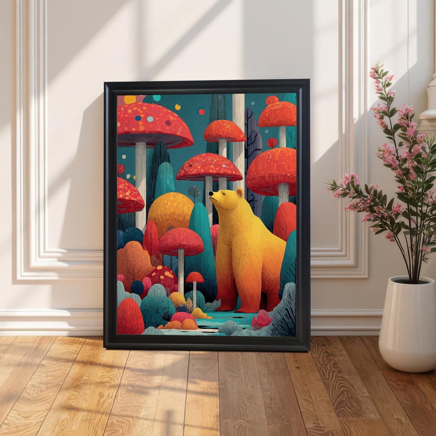 A framed art print featuring a golden bear among large, colorful red mushrooms and trees. The Black frame is leaning on a light wood floor against a white paneled wall, with a tall plant in a white vase on the right.