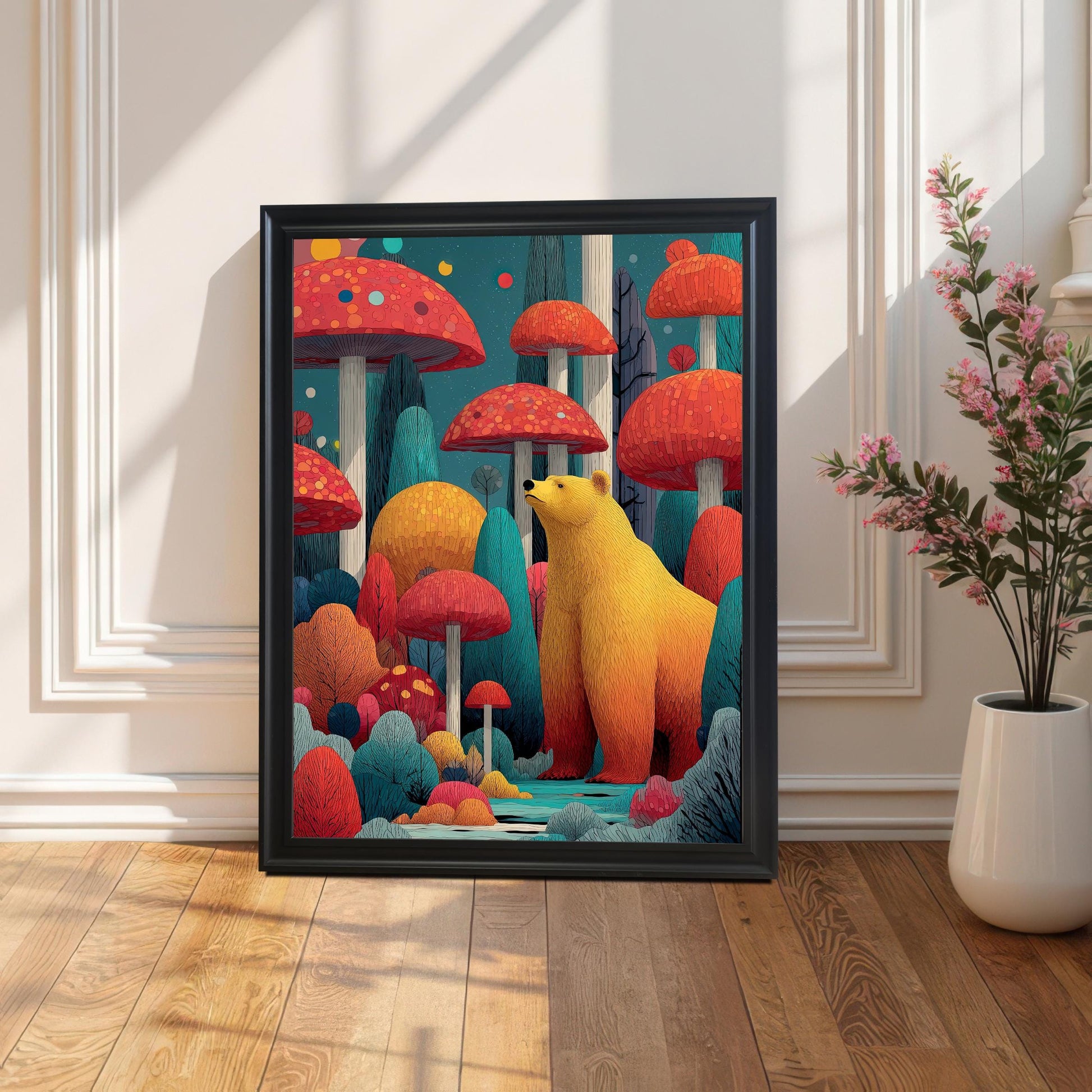 A framed art print featuring a golden bear among large, colorful red mushrooms and trees. The Black frame is leaning on a light wood floor against a white paneled wall, with a tall plant in a white vase on the right.