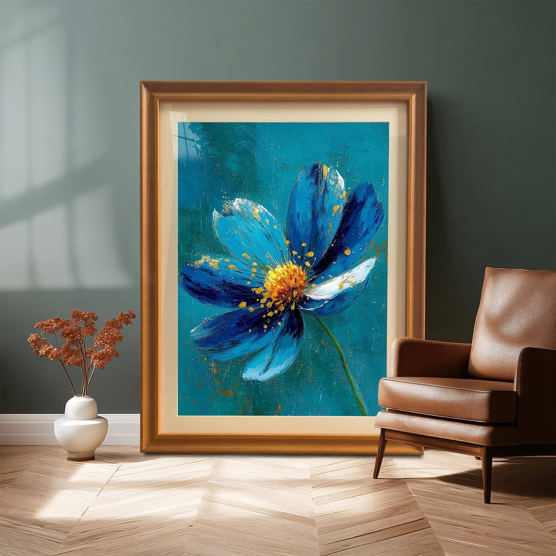 A very large framed print of the blue and gold flower, set in an Orange-toned wooden frame, leaning on a wood floor against a dark teal wall next to a brown leather armchair.