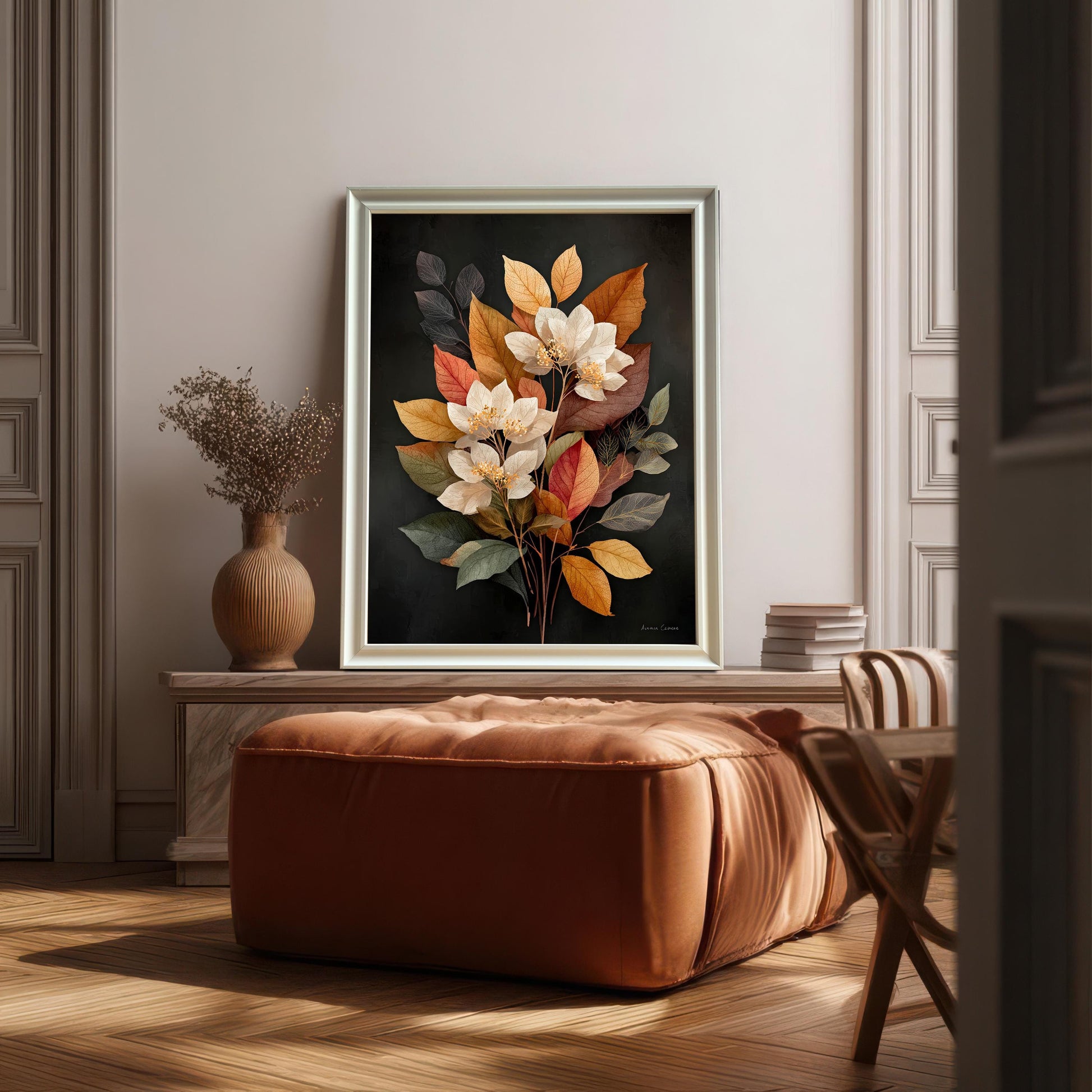 A framed art print of the autumn floral bouquet art hangs on a warm gray wall in a classic, elegant room. The frame is a light metallic or silver color and the art is displayed above a large, brown leather ottoman, showcasing a sophisticated interior design style.