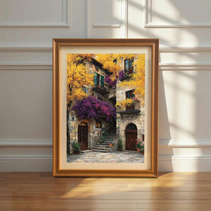 Framed art print with a gold/orange wood frame leaning against a white wainscoted wall. The painting is a vibrant, textured depiction of a Mediterranean stone building covered in bright yellow and purple foliage.