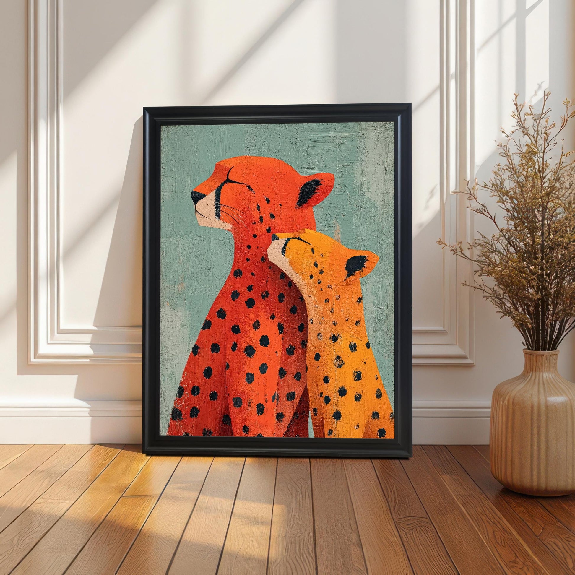 The framed 'Cheetah Love' art print, in a Black Frame, leaning on a light wooden floor against a white paneled wall. Strong, diagonal sunlight casts dramatic shadows. A tall, light brown vase with dried grasses is visible on the right.