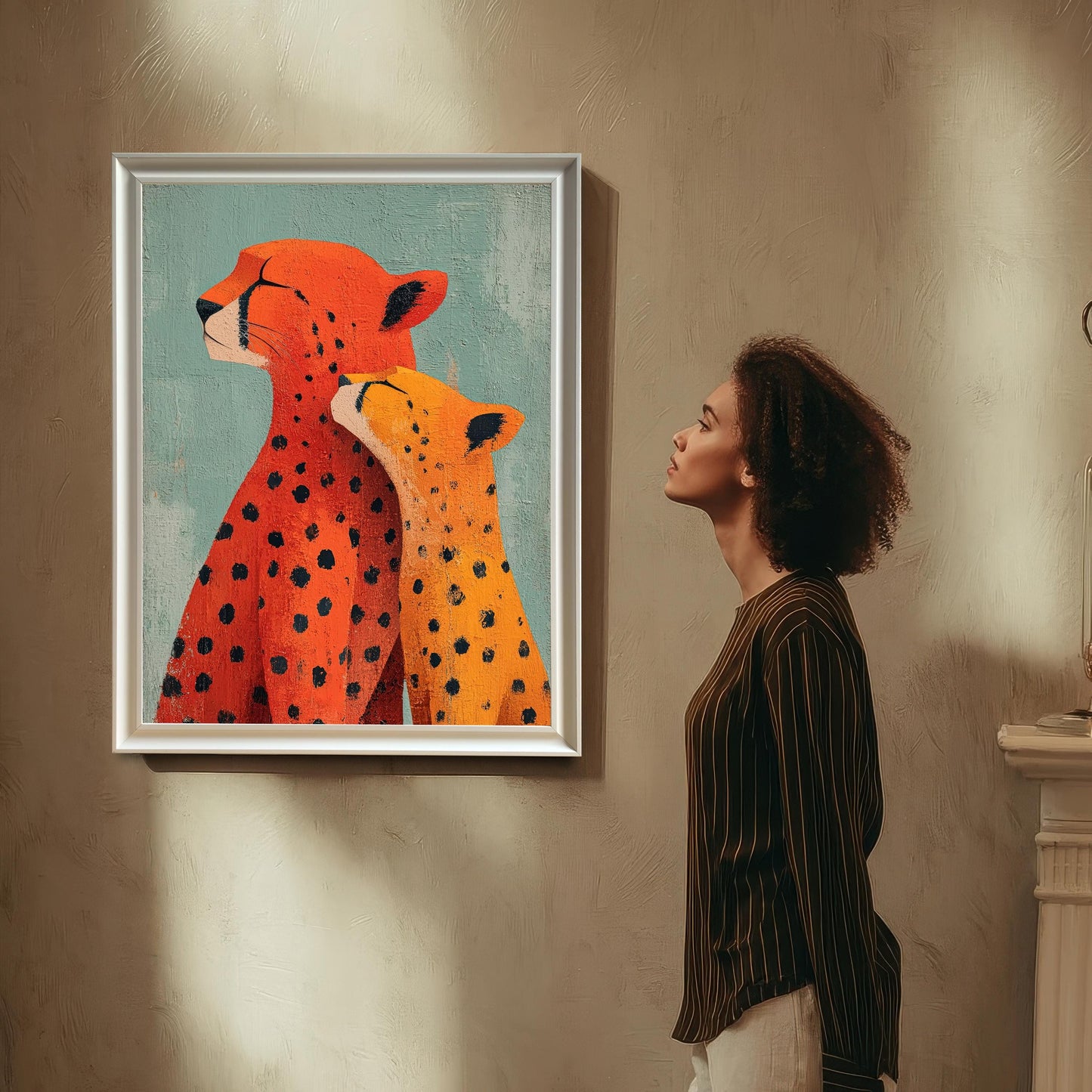 A woman with curly hair is standing and looking up at the framed 'Cheetah Love' art print, which is hanging on a textured beige wall. The art is displayed in a thin White/Silver Frame with a mount.