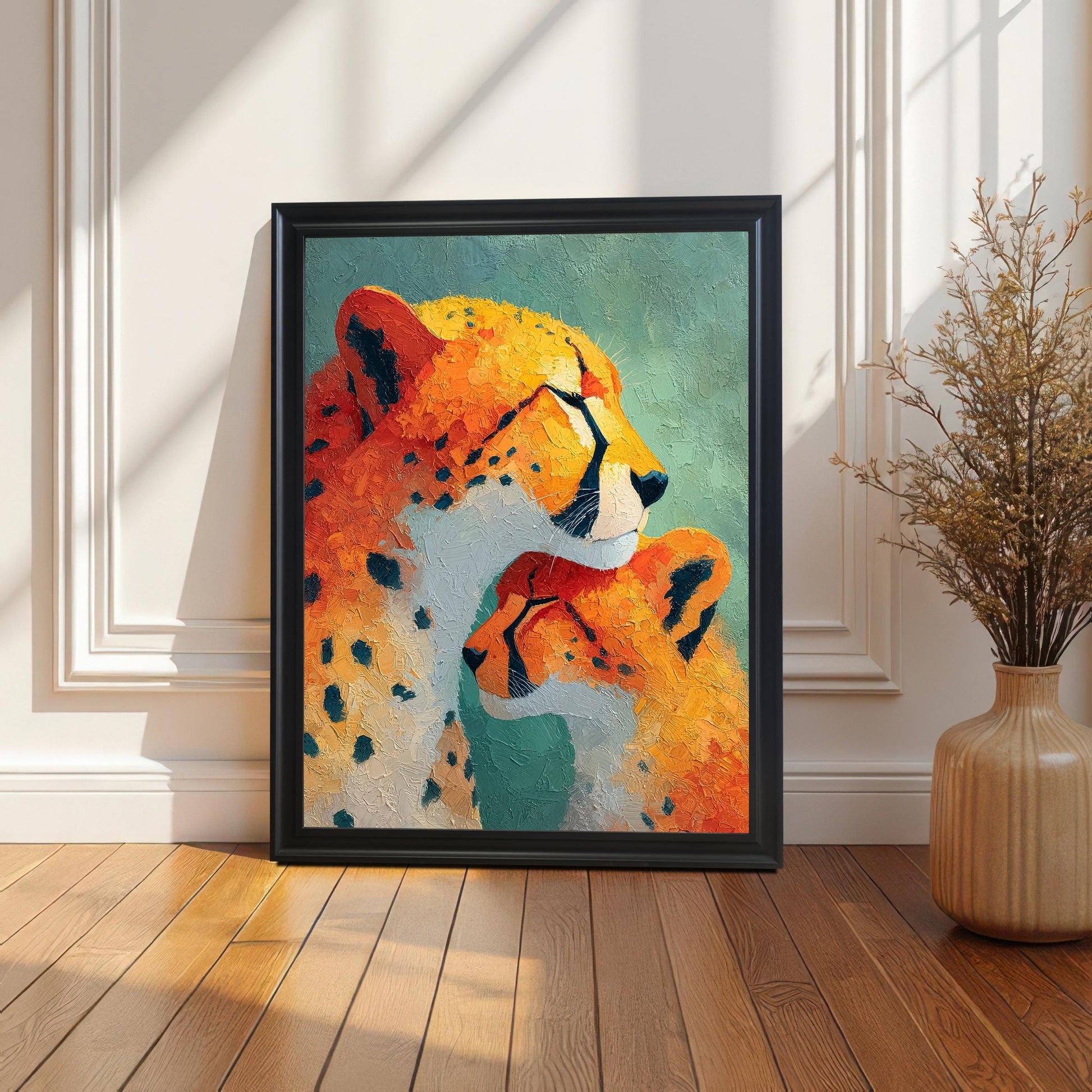 Lifestyle shot of the cheetah and cub art print with a Black wood frame, leaning on a light-colored wood floor against a white paneled wall. Natural sunlight casts strong shadows, and a dried floral arrangement in a beige vase sits next to the print.