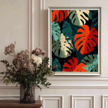 A lifestyle shot of the bold Monstera leaf art print with a thick White wood frame, hanging on a sophisticated white paneled wall. A vase with dried floral and eucalyptus arrangement sits on a table to the left.