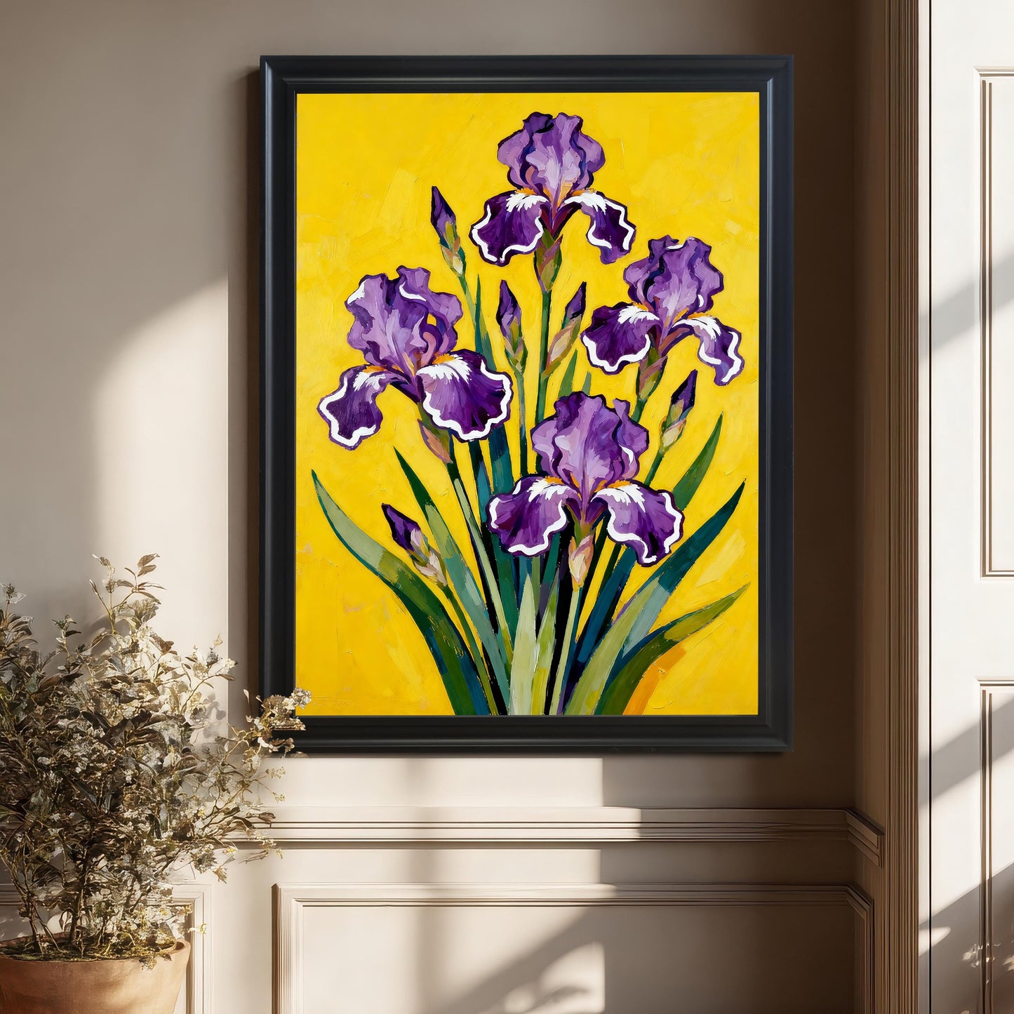 A large Black framed art print featuring a vibrant painting of purple Irises on a bright yellow background, hanging on a beige wall above a chair rail, with a potted plant on the left.