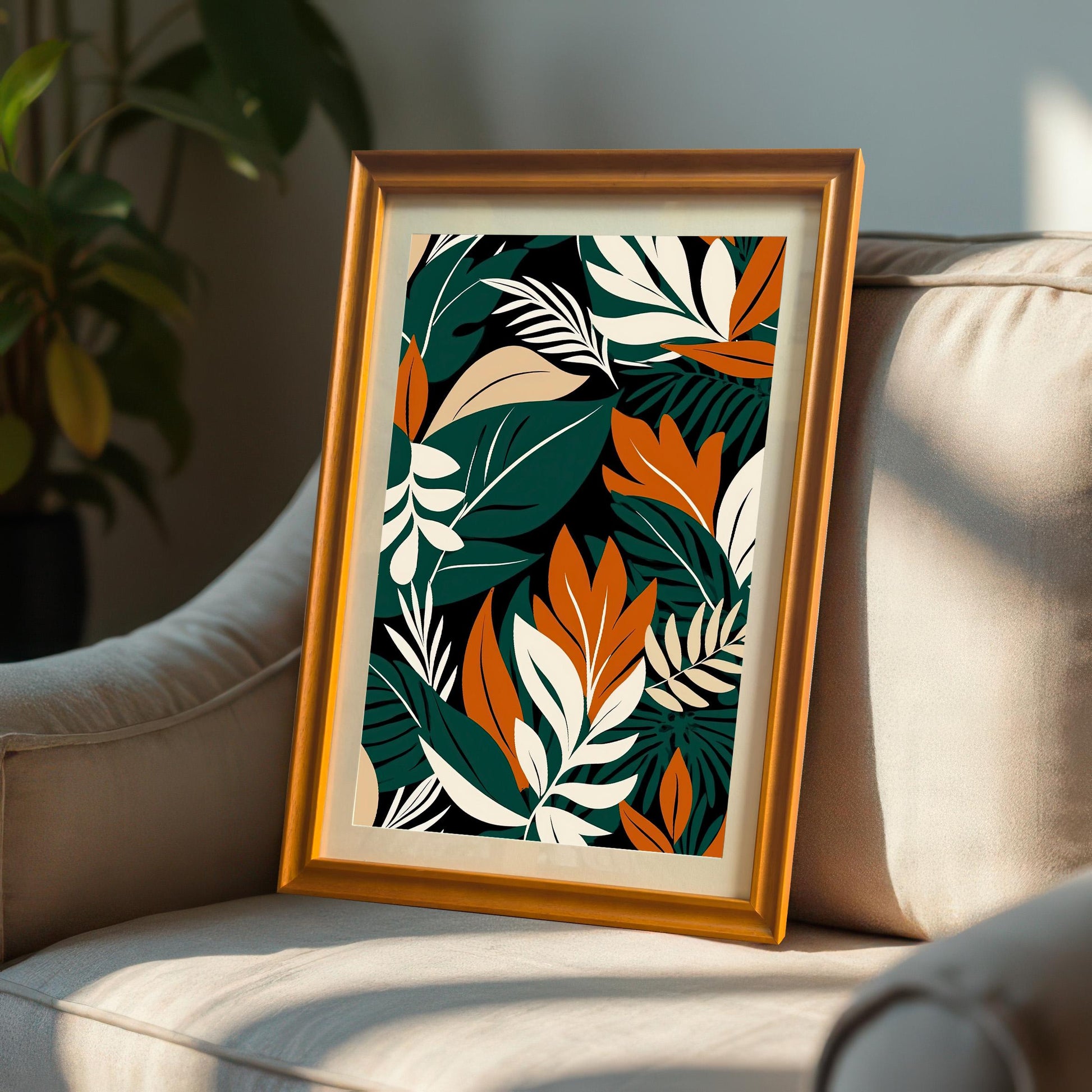 Abstract tropical leaf art print in a Gold/Orange frame, leaning on the arm of a light-colored armchair in a sunny room.