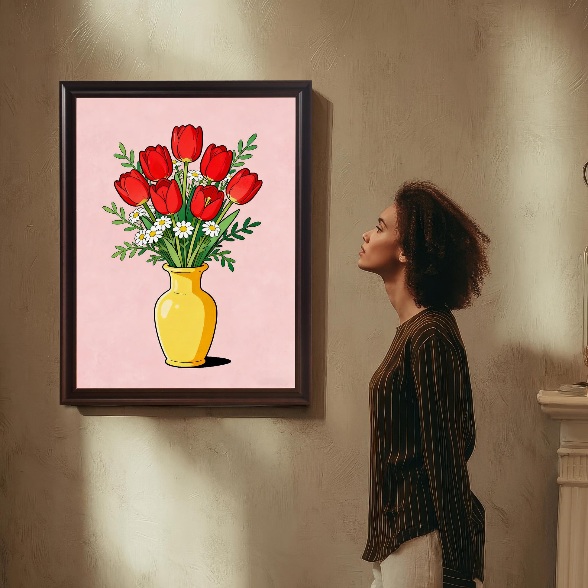 A woman with curly hair, wearing a striped shirt, stands and admires a large framed art print hanging on a textured wall. The art features a stylized bouquet of red tulips and white daisies in a yellow vase against a pink background, framed in a dark brown/coffee-colored wood frame.