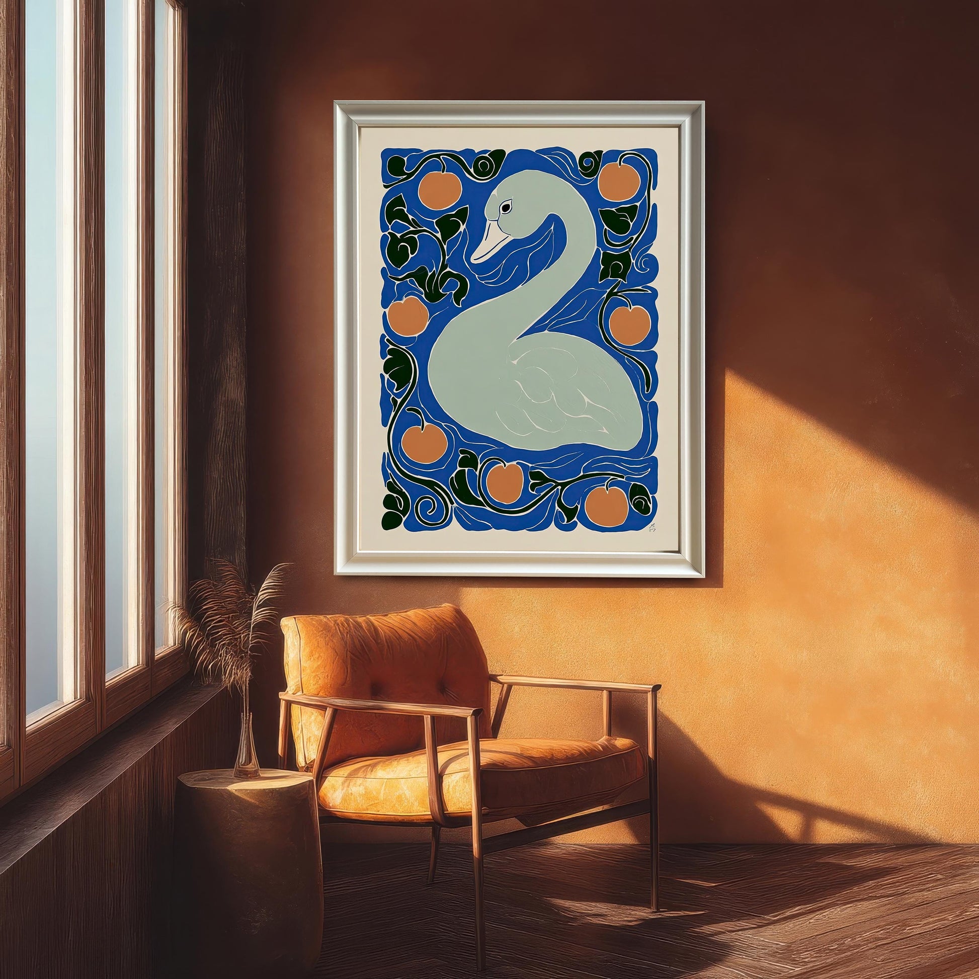 The framed swan print in a thin silver/white frame, hanging on a textured orange wall in a room with a large window and a brown leather armchair.