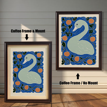 Two framed prints of the swan artwork against a wooden plank wall. The print on the left is a Coffee Frame & Mount (dark brown frame with a white border/mat). The print on the right is a Coffee Frame / No Mount (dark brown frame where the art fills the frame).
