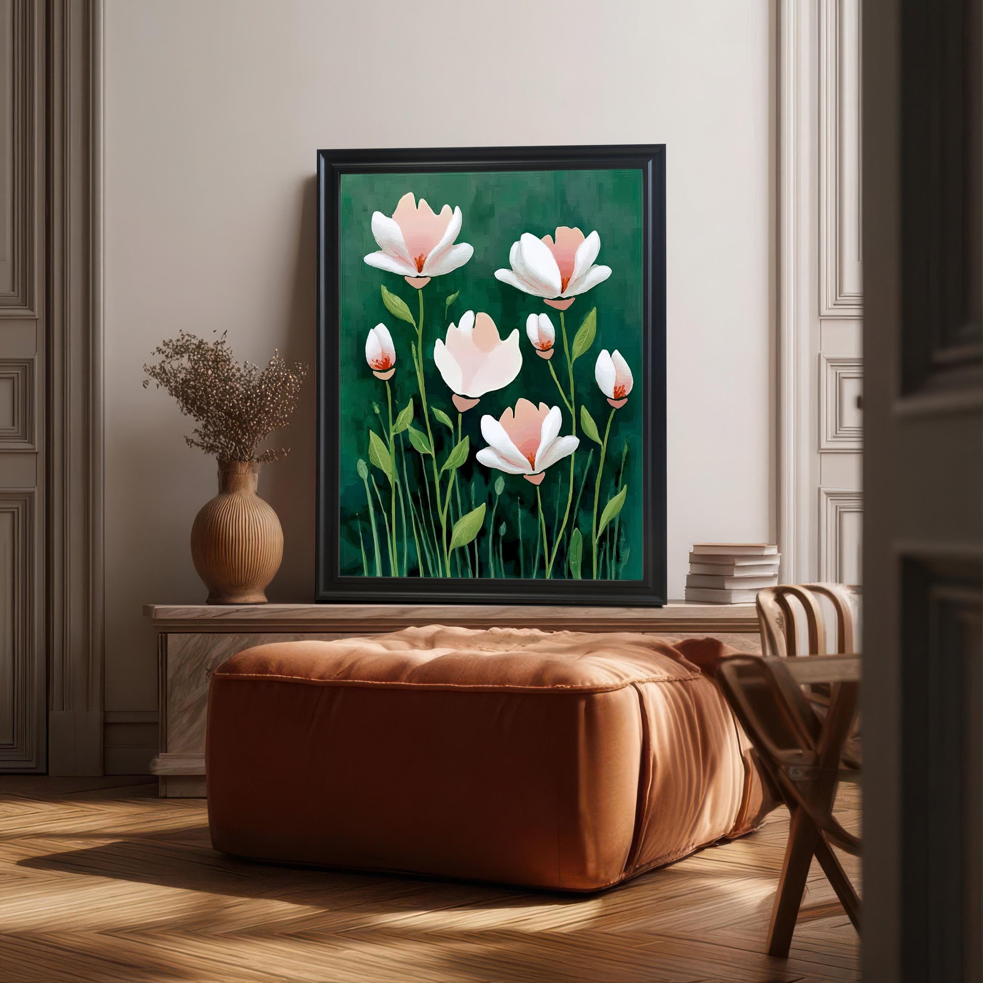 The abstract floral print is in a black frame, leaning against a pale mantlepiece above a large, square, burnt-orange leather ottoman in a sunlit, elegant room.