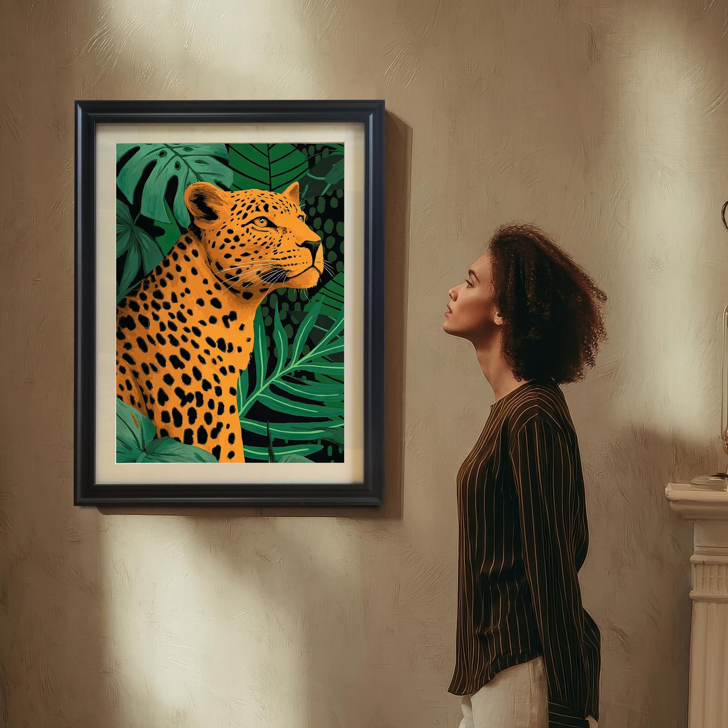 Lifestyle photo showing a woman with curly hair, wearing a striped shirt, looking up at the framed leopard art print hanging on a textured, light brown wall. The print is framed in black with a white mat (mount).