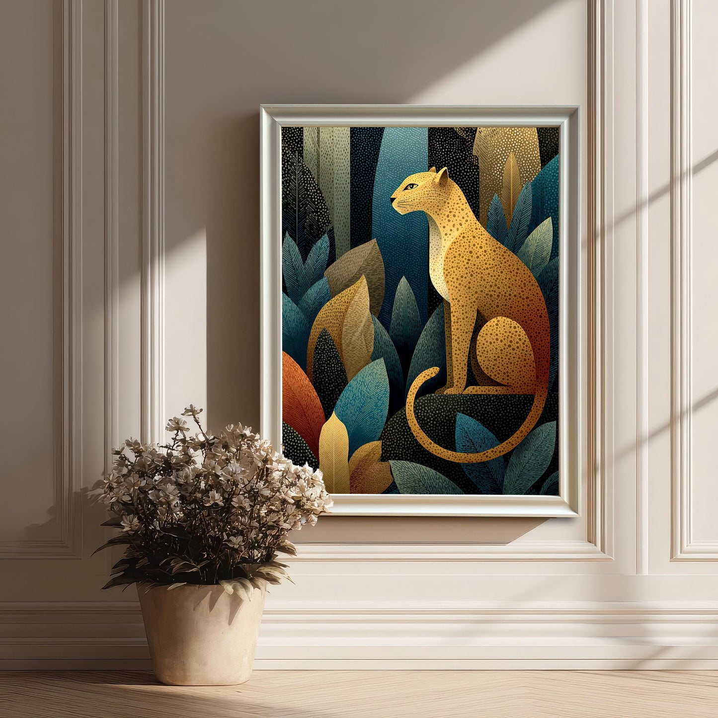 A framed art print of a golden leopard in a jungle of stylized leaves, shown with a thick white frame leaning on a light wood floor next to a white paneled wall and a potted bouquet of dried flowers.