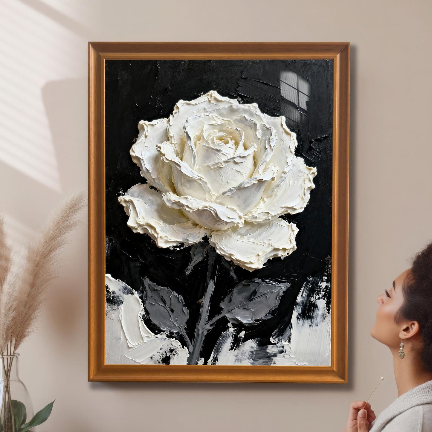 A framed print of the textured white rose painting with an Orange wood frame, hanging on a neutral wall. A woman stands in the foreground, admiring the high-contrast black and white artwork.