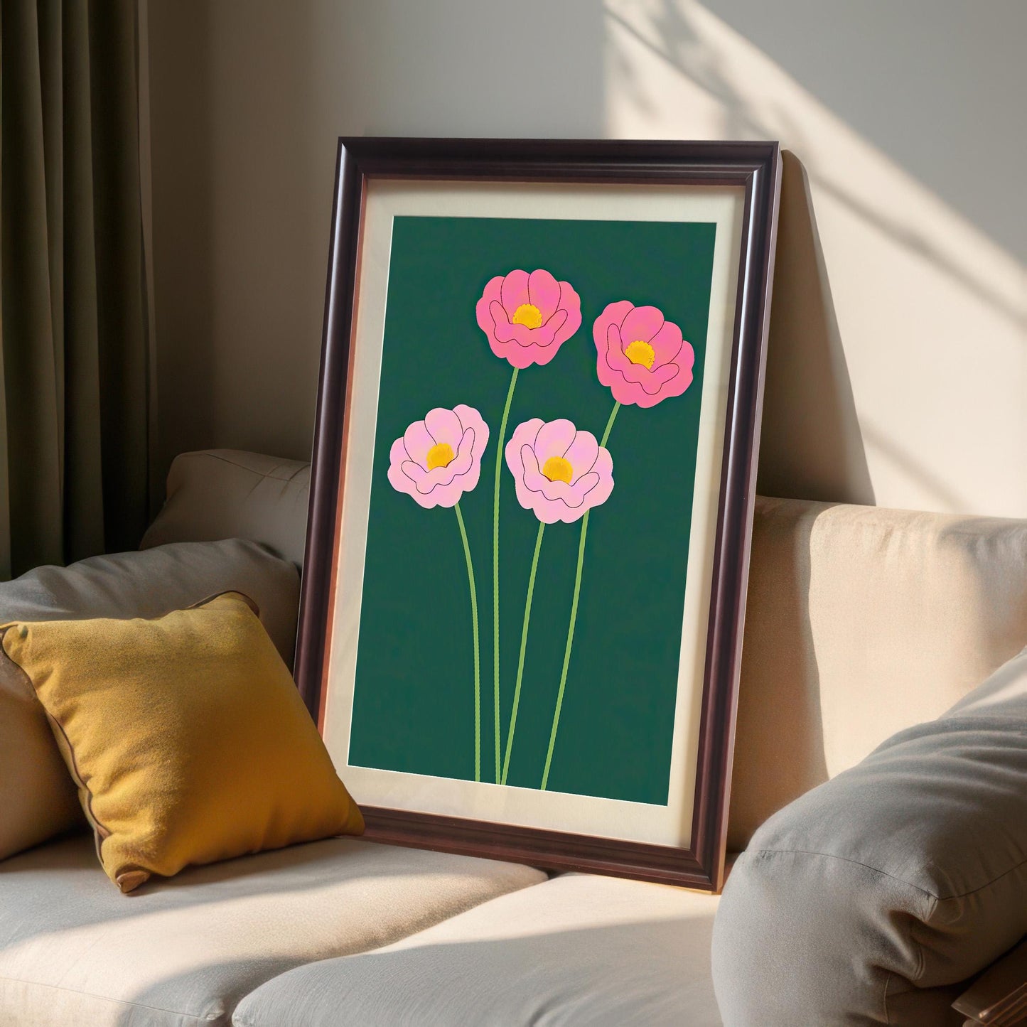 The pink floral art print in a dark Coffee Frame with a mount/mat, resting on a light beige sofa next to a yellow throw pillow. The art features bright pink flowers on a dark green background.