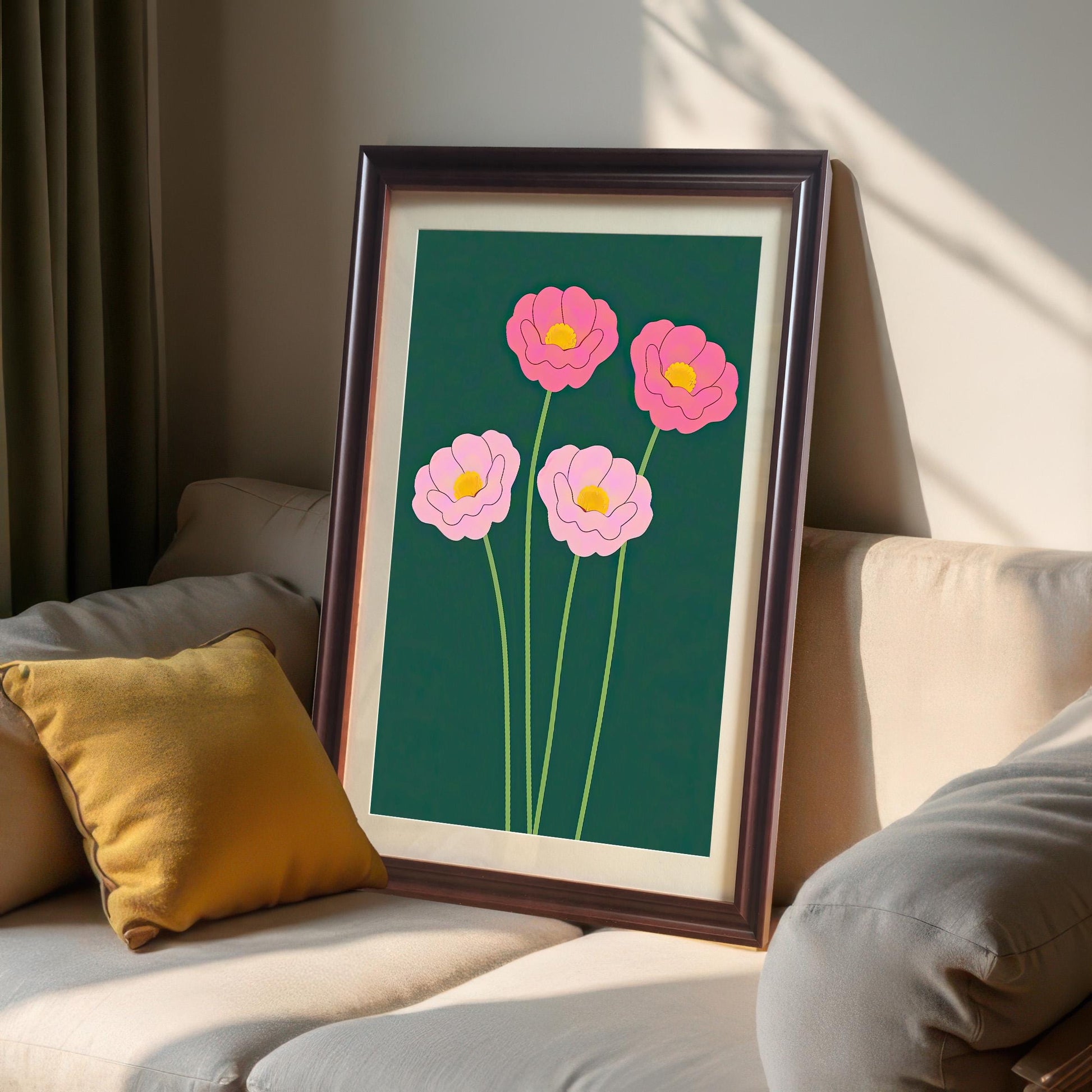 The pink floral art print in a dark Coffee Frame with a mount/mat, resting on a light beige sofa next to a yellow throw pillow. The art features bright pink flowers on a dark green background.