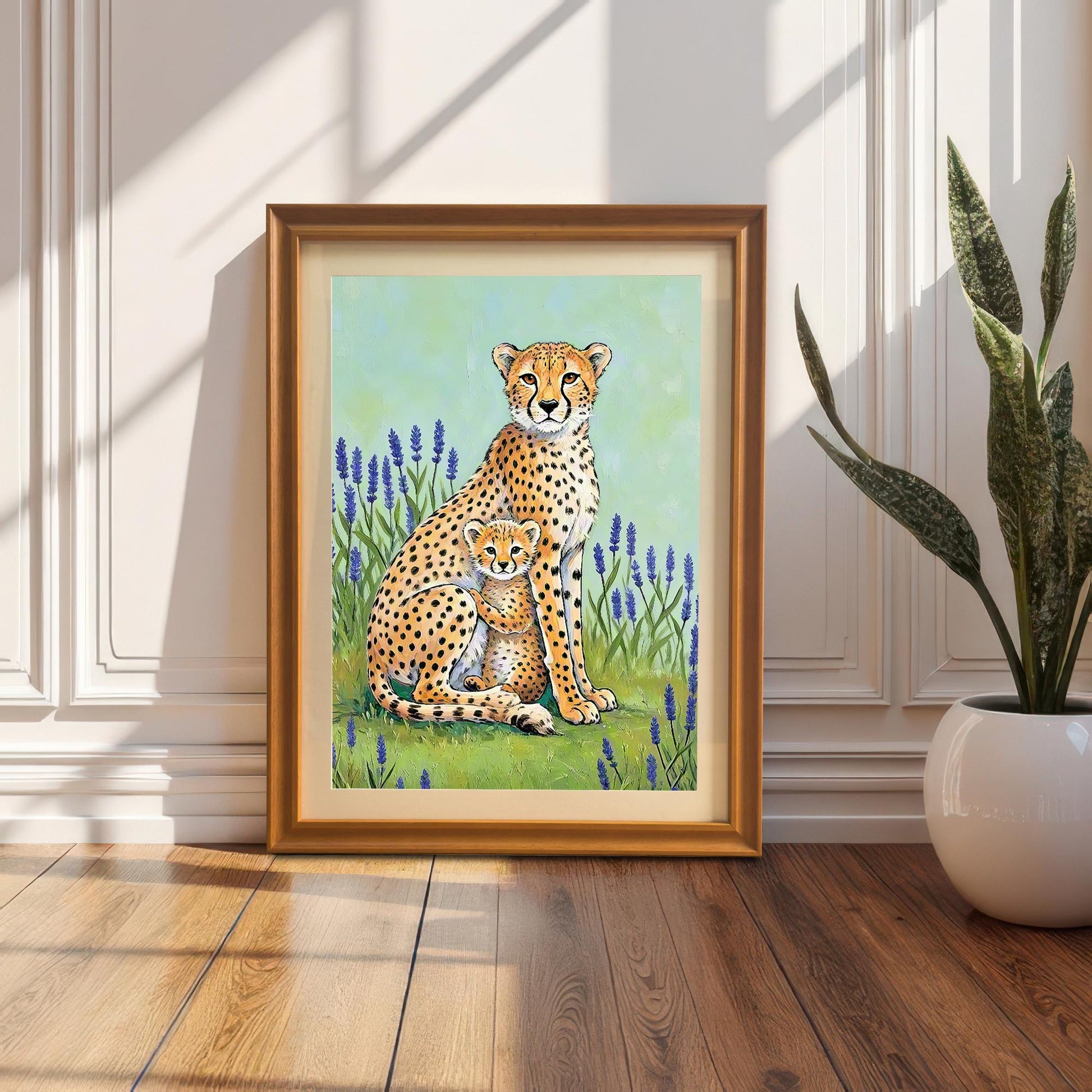 Lifestyle image of the cheetah mother and cub framed art print in a gold/Orange Wood Frame, leaning on a wood floor against a white paneled wall next to a potted snake plant. Strong sunlight and shadows create a warm effect.