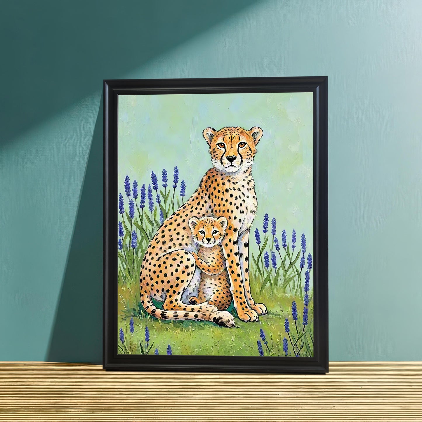 A close-up studio shot of the cheetah mother and cub art print in a Black Wood Frame, leaning on a light wood surface against a teal-colored wall. Sunlight and shadow highlight the colorful illustration.