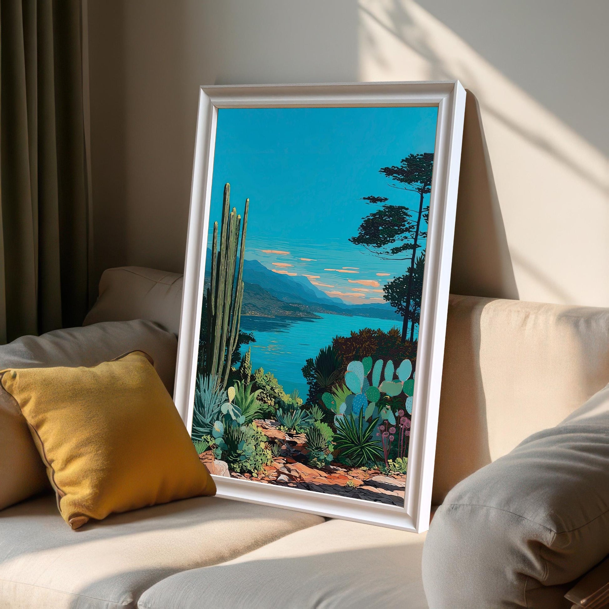 The framed artwork, with a white frame, is leaning on a light-colored sofa next to a yellow pillow, bathed in sunlight coming through a window. The art depicts a bright blue lake, mountains, and desert plants like cacti.