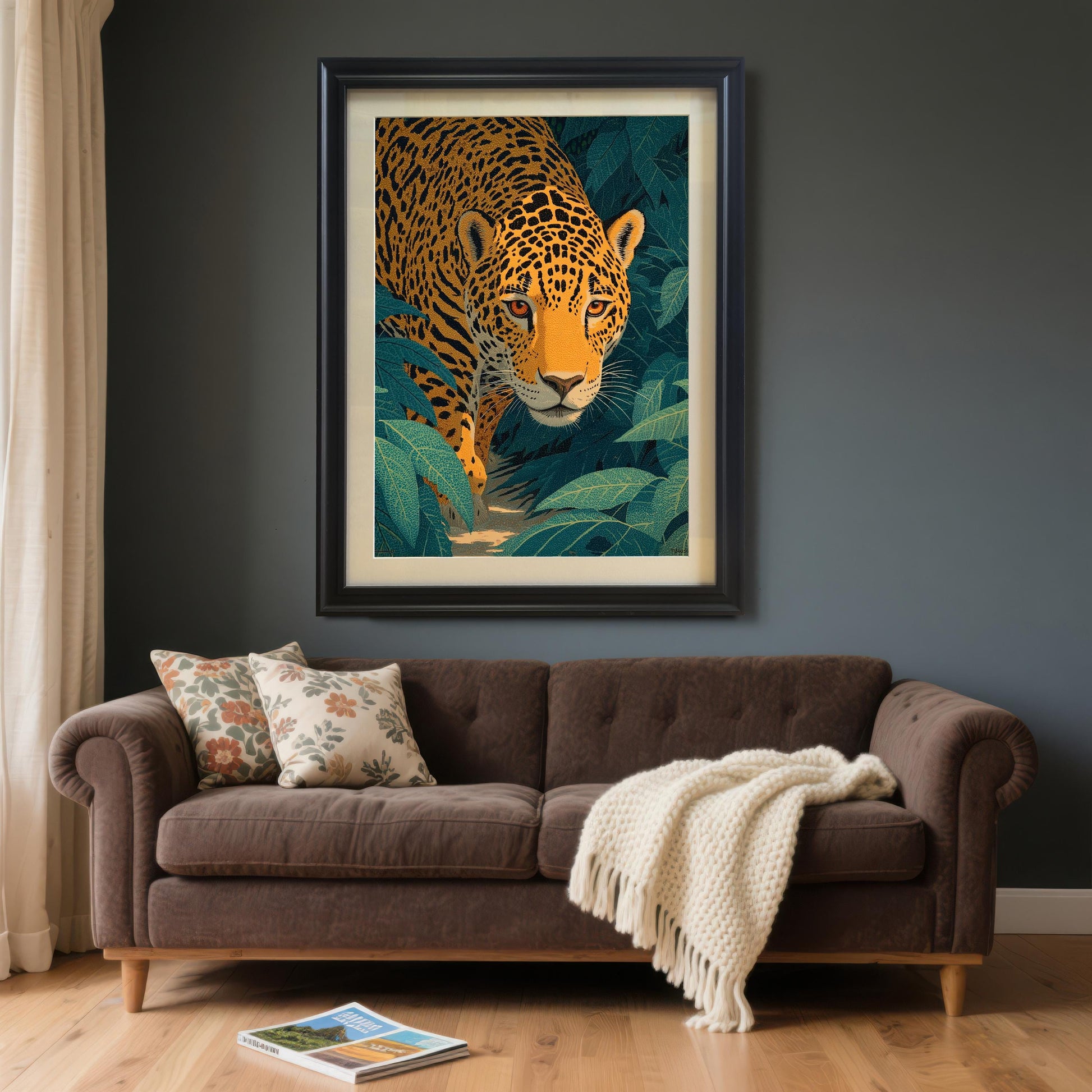 Large framed artwork of a jaguar in the jungle, in a Black frame (with mount). It is hung on a dark gray wall above a brown velvet sofa with throw pillows and a white blanket.