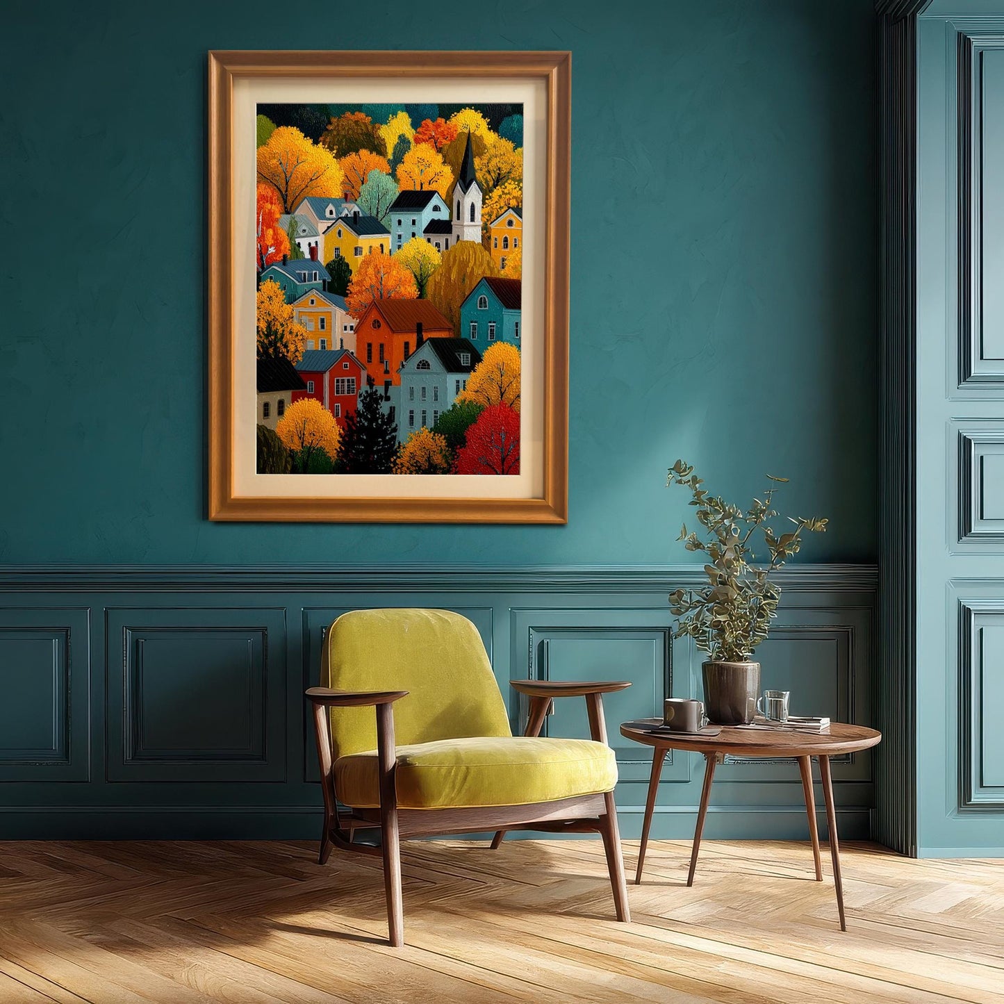 A framed print of a colorful autumn village scene hanging on a deep teal wall, positioned above a yellow armchair next to a small side table.