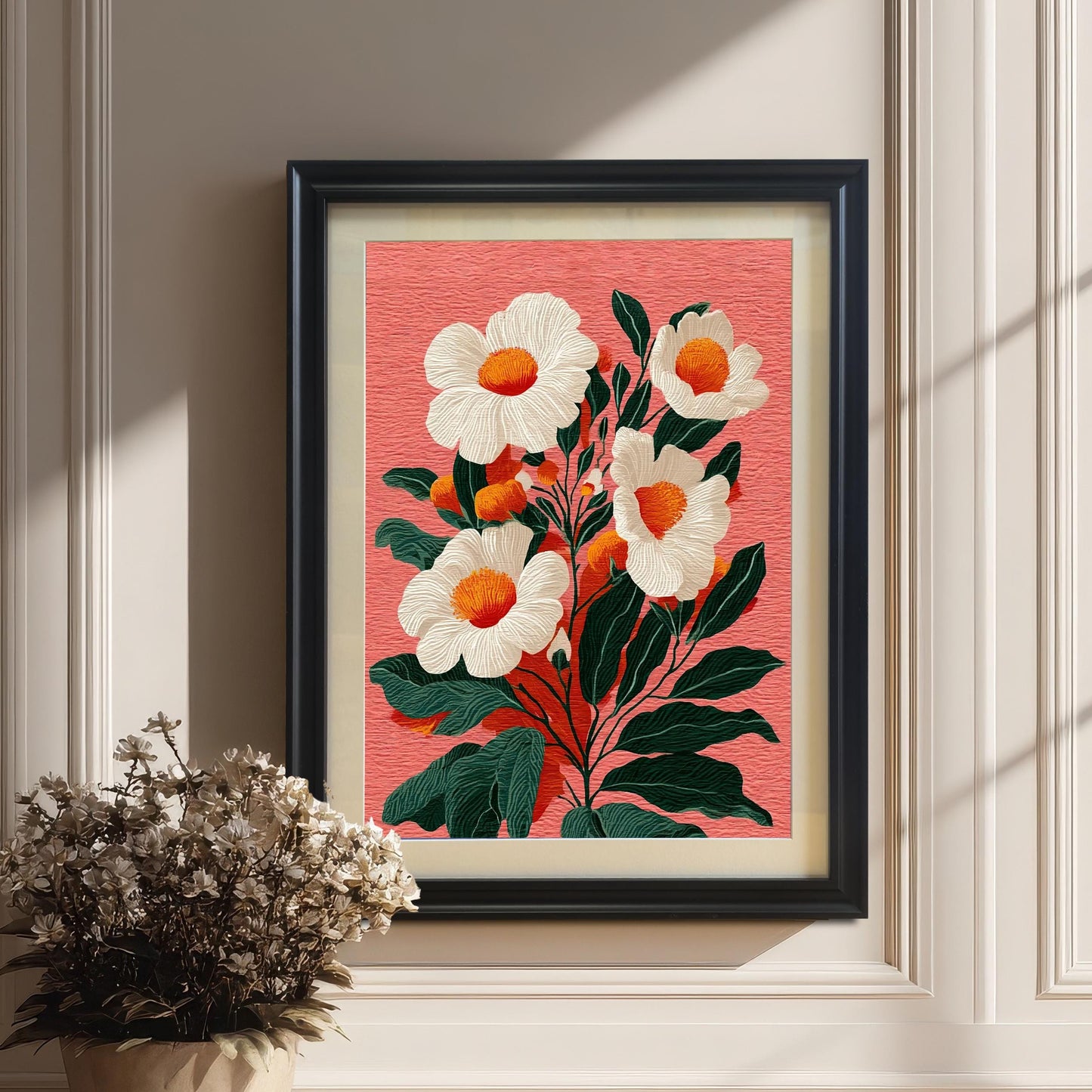 A framed floral print with a black frame and a beige mount hanging on a white paneled wall. A potted bouquet of dried white flowers sits on the wooden floor next to the art.