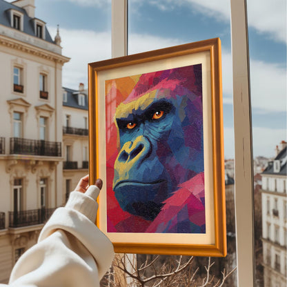 A hand in a white sweater holds up the framed gorilla print against a background of a sunny city view with buildings and a bright blue sky. The print has a bright orange-gold frame.
