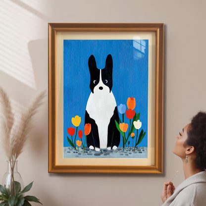 Framed art print of a black and white dog with tulips hanging on a beige wall. A woman with an afro is standing nearby, looking up at the artwork. The frame is a gold/orange color.
