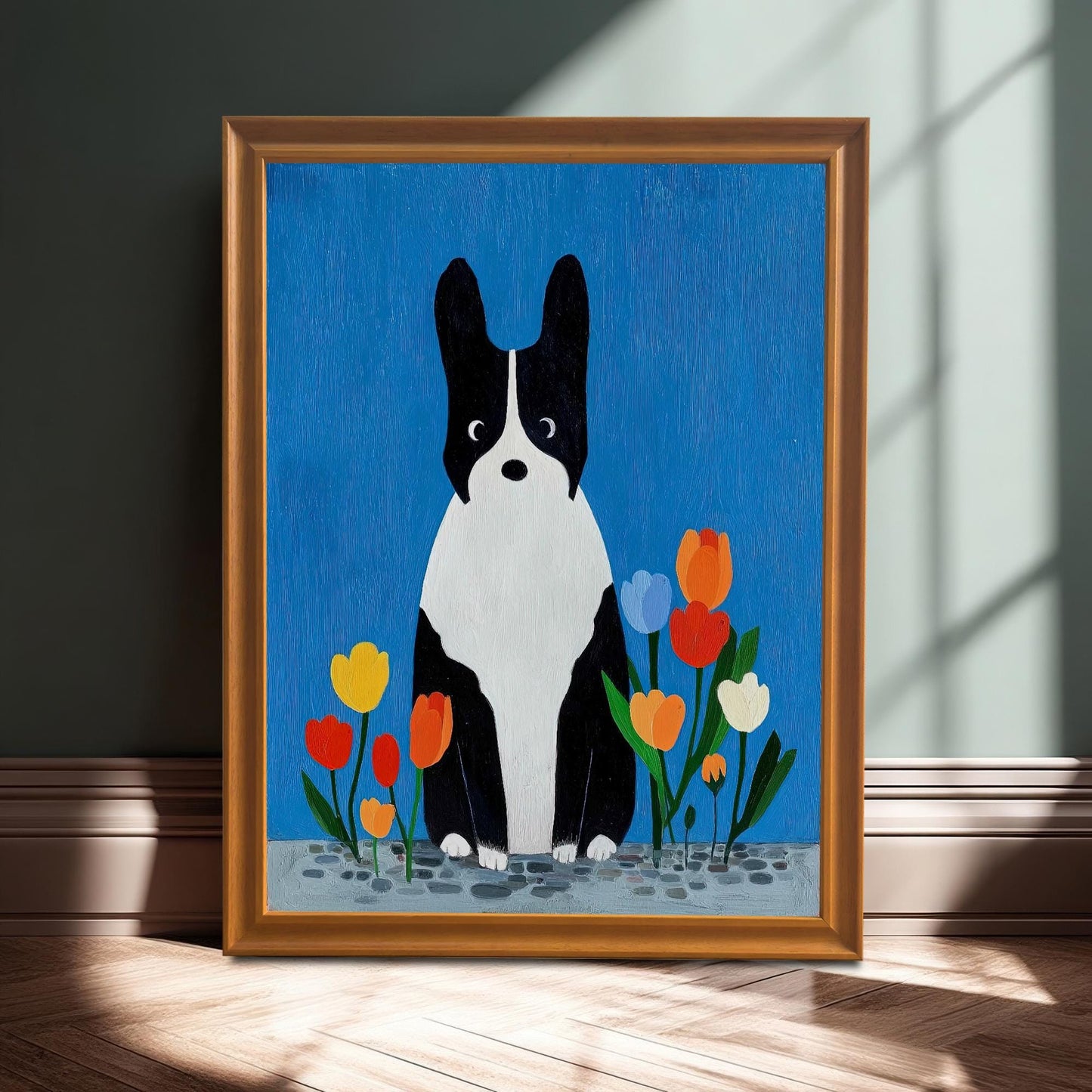 Close-up of a framed art print featuring a black and white dog sitting among colorful tulips against a blue background. The frame is Orange/Gold and the print is shown leaning on a wooden floor against a dark green wall, bathed in natural light.