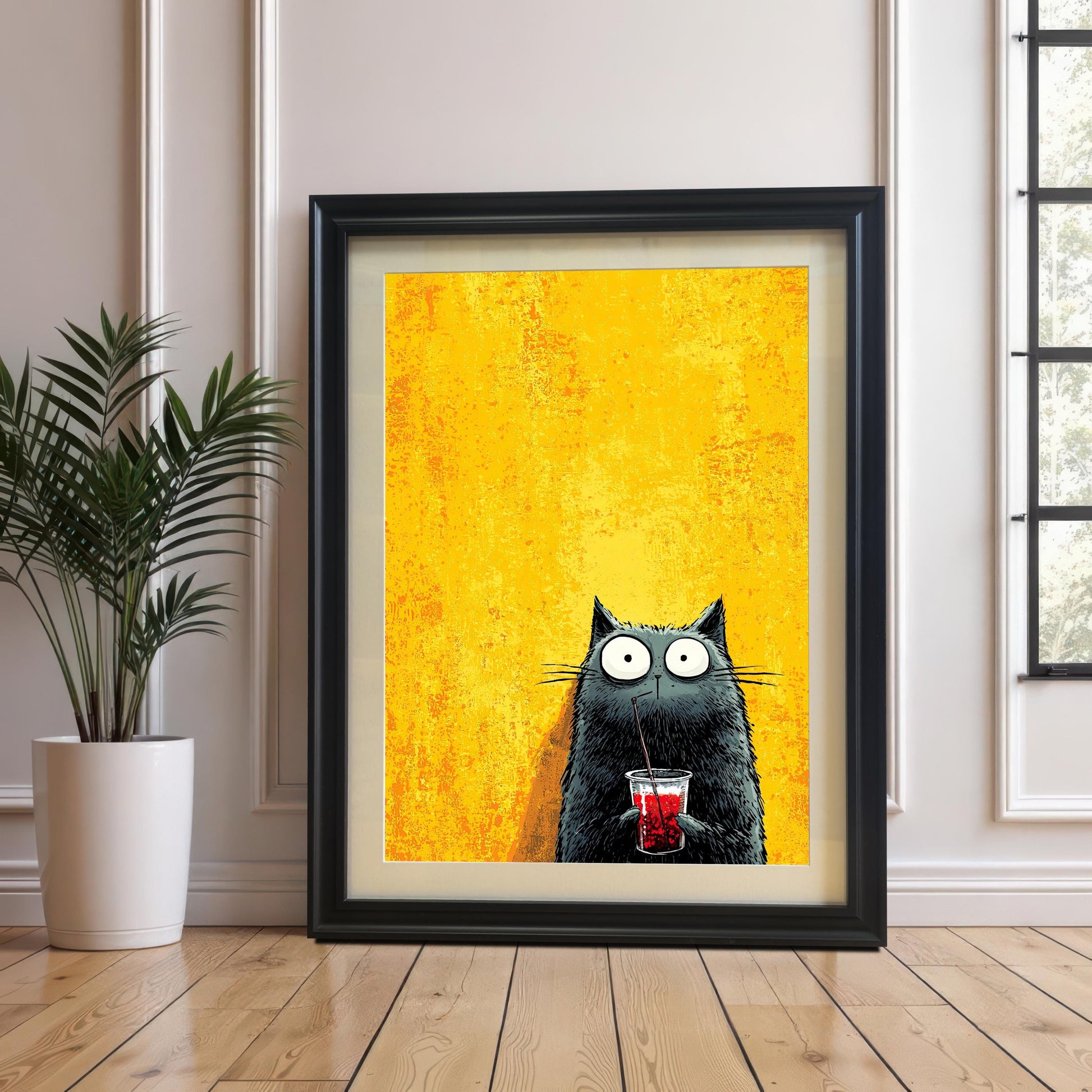 The black cat print is displayed in a large, thick black frame with a light mat (mount), leaning against a white wainscoted wall next to a potted houseplant.