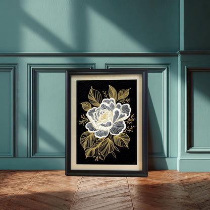 A framed black and gold floral print, featuring a white and gold stylized flower on a black background, leaning against a teal wainscoted wall and wooden floor, illuminated by a sunbeam.