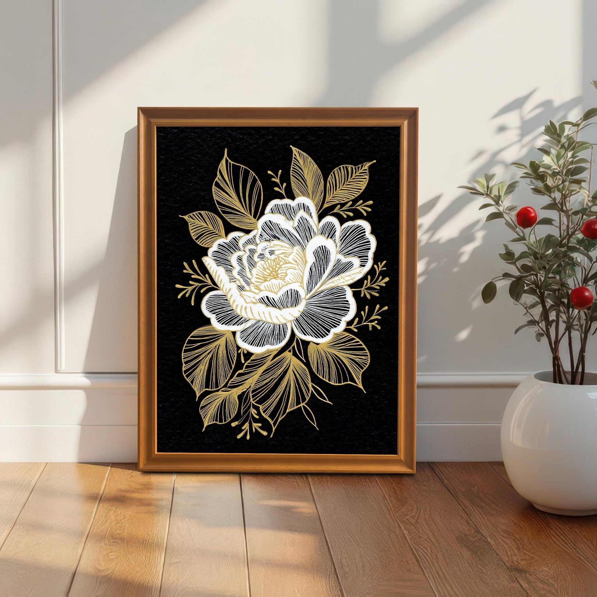 The floral print in a dark wood frame, leaning against a white wainscoted wall next to a small potted plant with red berries.