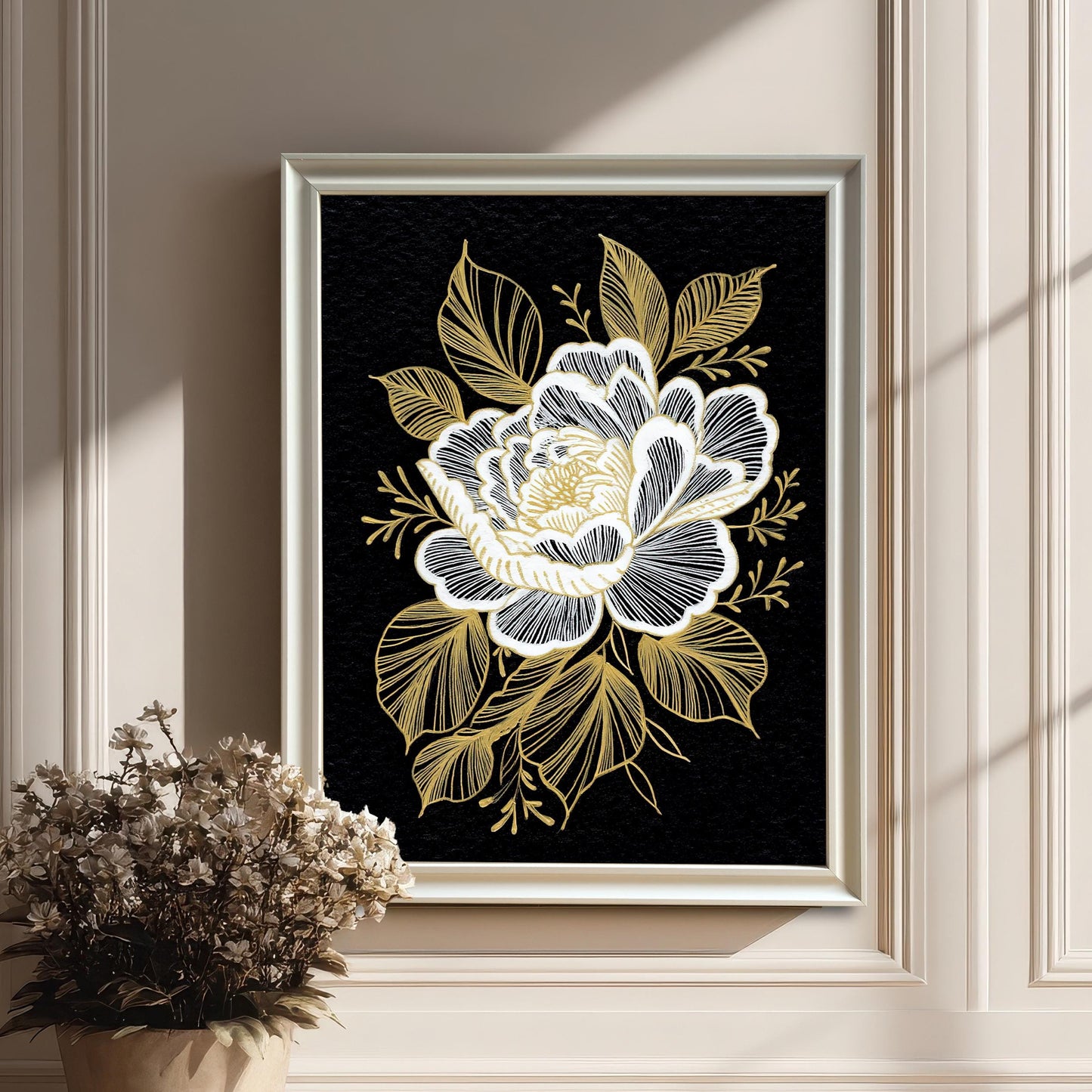 The floral print in a white frame, hanging on a white wainscoted wall next to a pot of dried flowers, with strong vertical shadows from a nearby window.