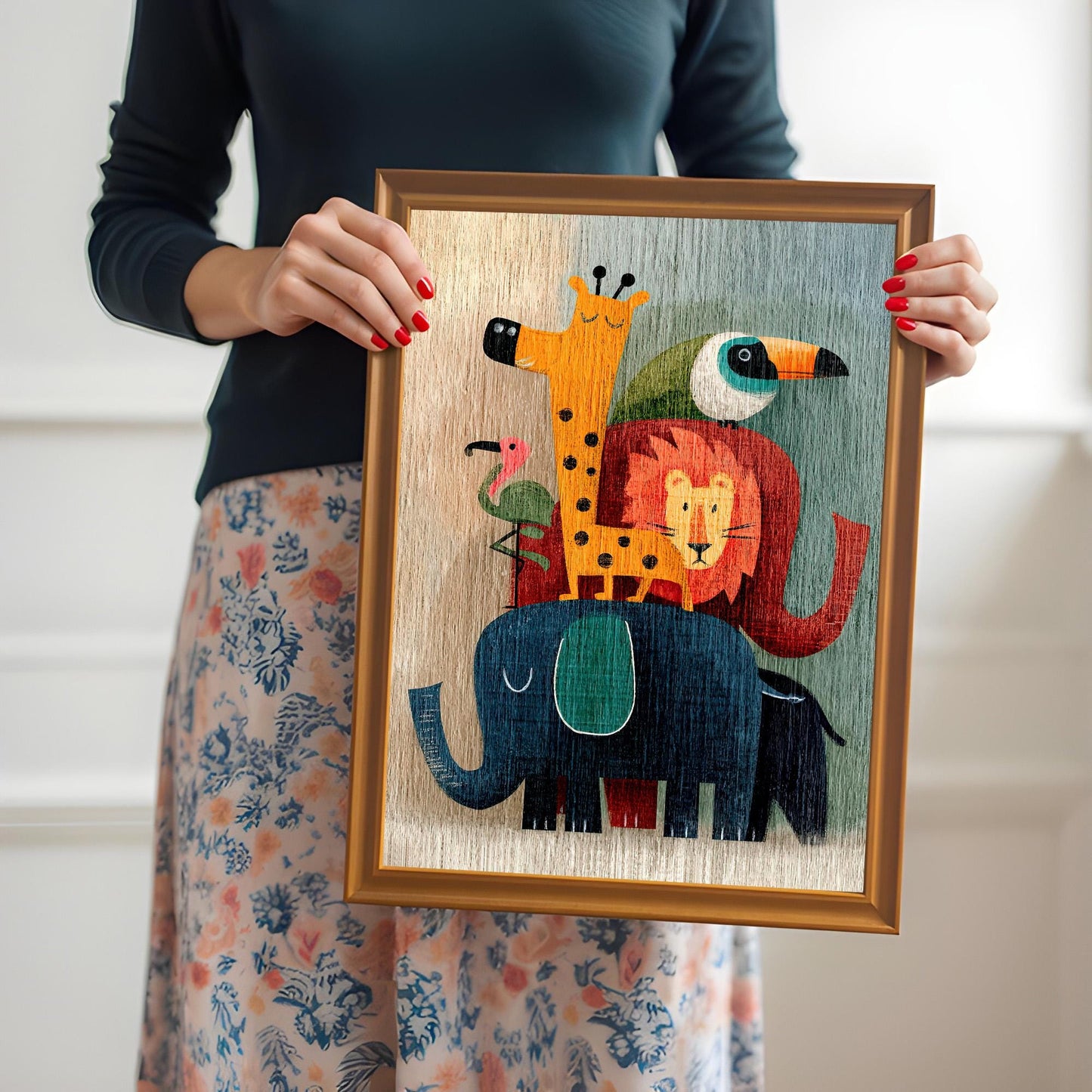A person wearing a dark top and floral skirt holds a medium-sized, orange-gold framed art print of the stacked cartoon animals with a light-colored mount.