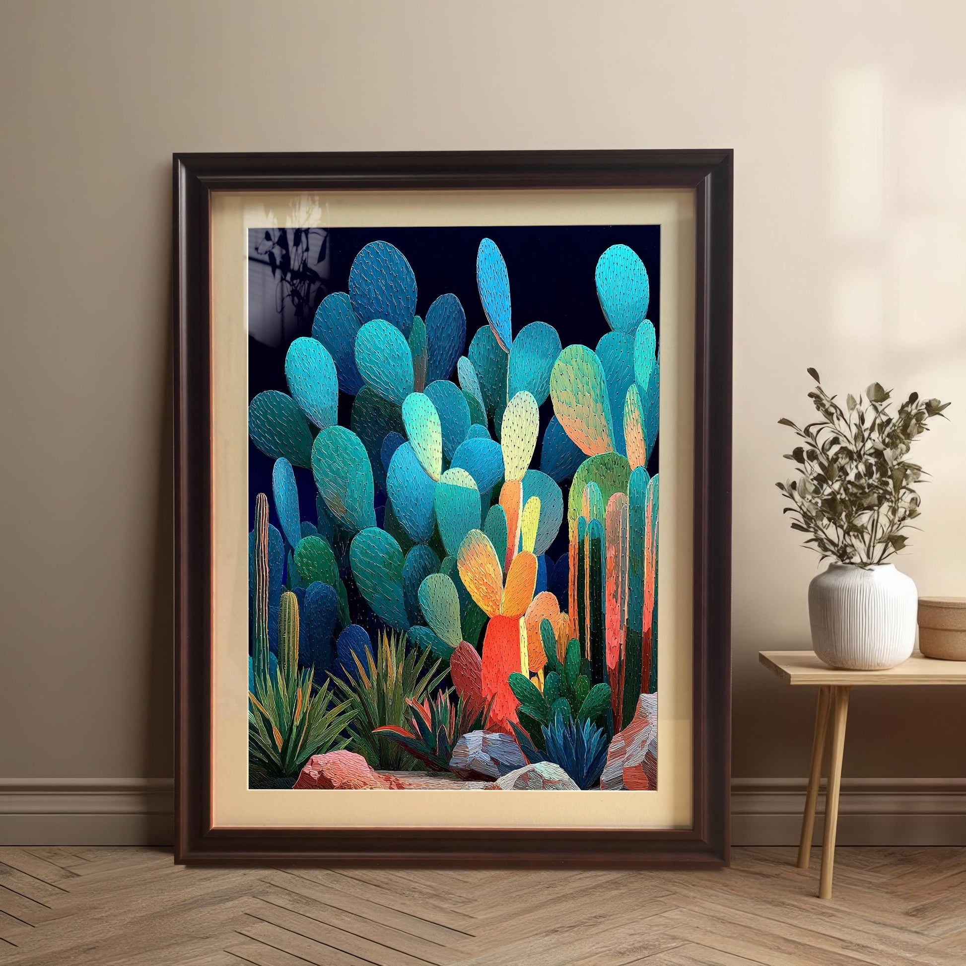 A large, dark brown (Coffee) framed art print of the abstract cacti with a mount, leaning against a light brown wall, next to a small side table with a decorative vase.