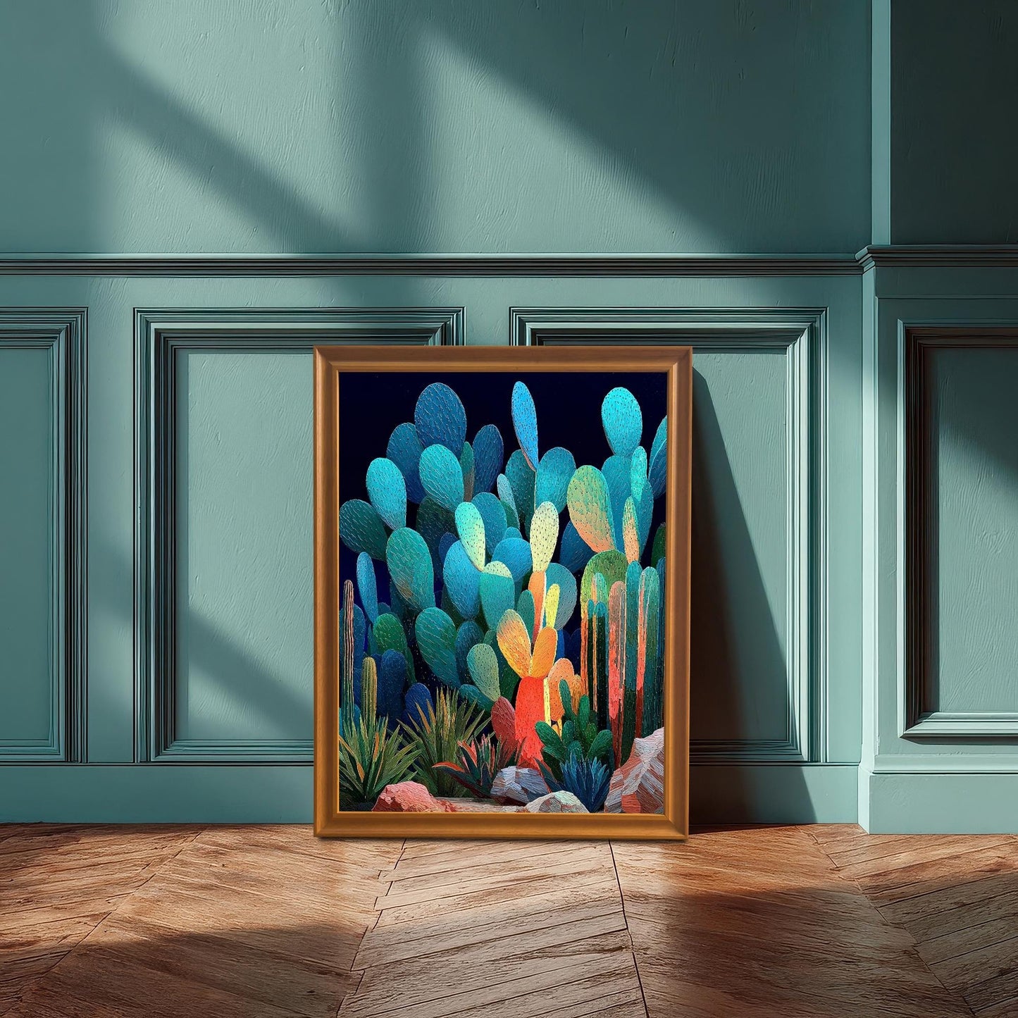 A framed, colorful abstract cacti print with an orange-gold frame, leaning against a teal wainscoting wall, with sunlight casting shadows on the floor and wall.