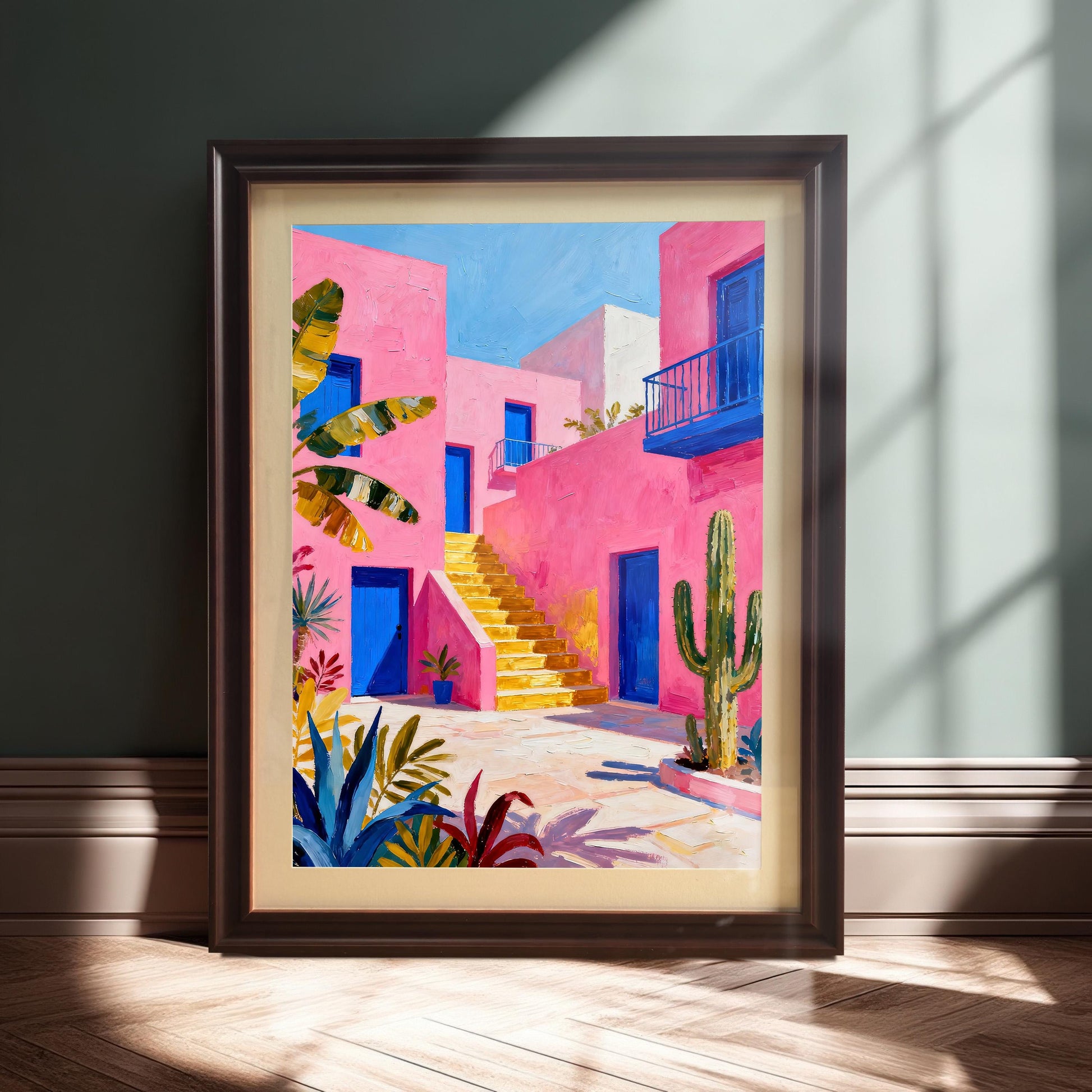 A framed print of a vibrant pink building with blue doors and yellow stairs, standing on a wooden floor against a dark green wall in a Coffee-colored frame with a Mount.