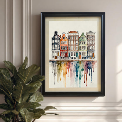 Watercolor print of colorful canal houses with a dripping rainbow reflection, framed in a black frame and hanging on a neutral paneled wall next to a large potted plant.