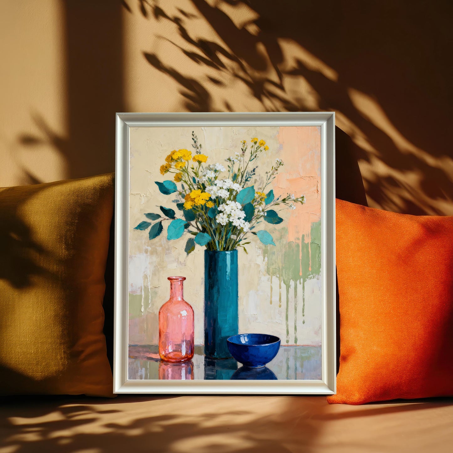 Still life art print in a White frame leaning between two pillows (mustard and orange) with dramatic leaf shadows cast on the wall.