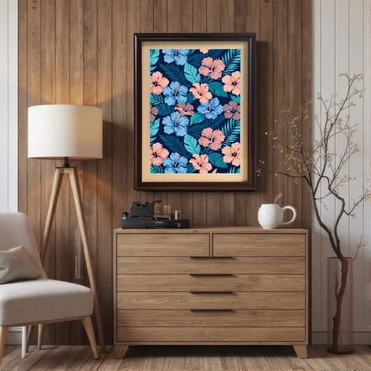 Framed tropical floral art in a Coffee wood frame hanging above a light wooden dresser, featuring pink and blue hibiscus, set in a room with wood paneling and a tripod lamp.