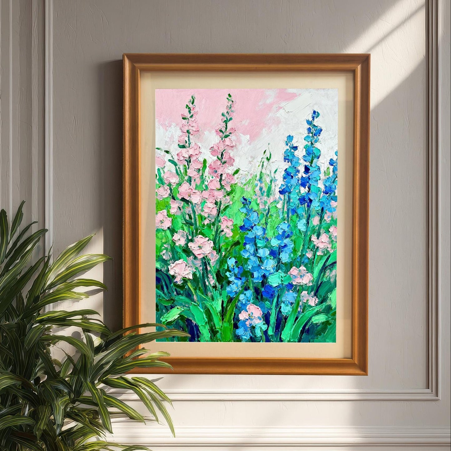Styled photo of the floral art print in a Brown wood frame, hanging on a light gray panel wall, next to a large potted palm plant.