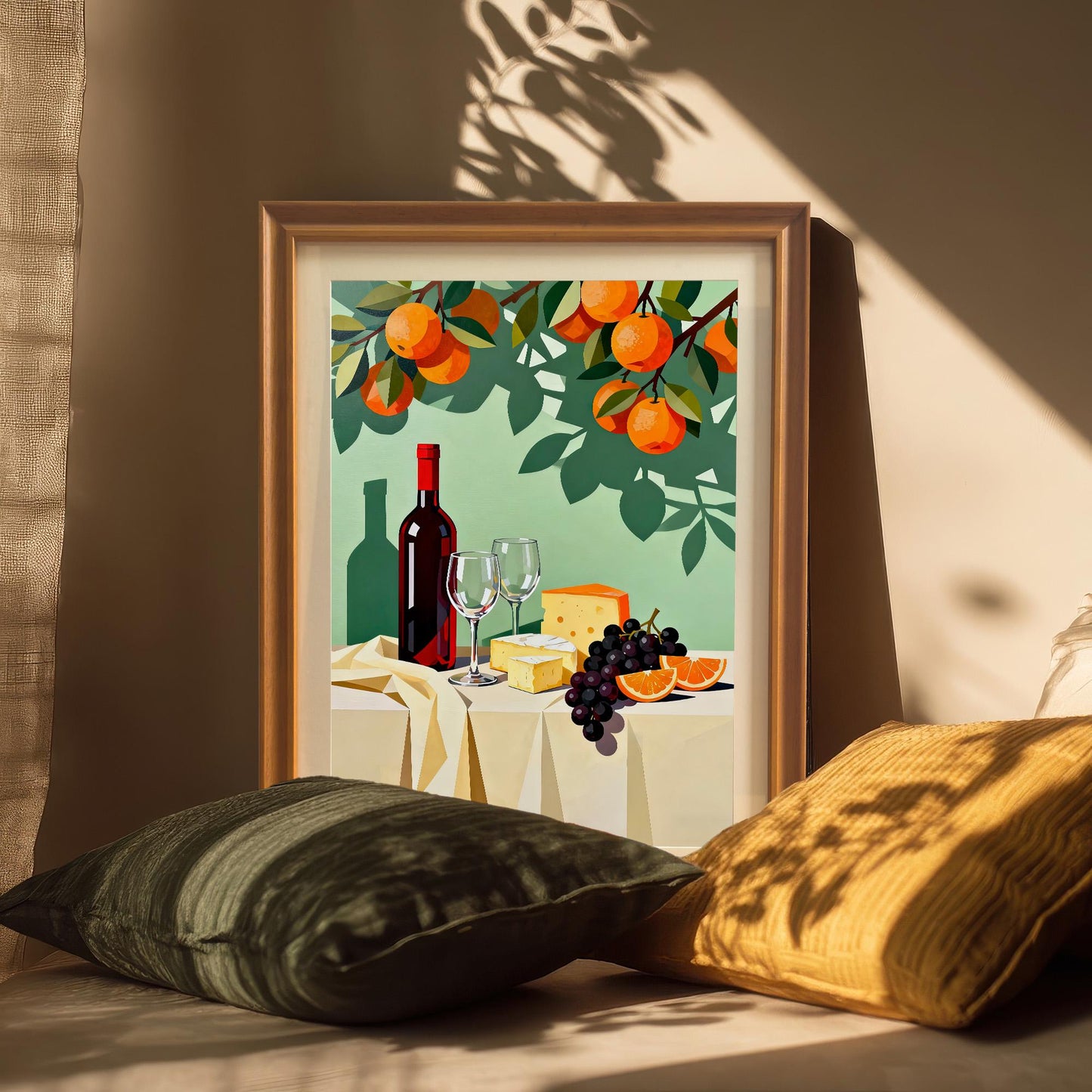 Styled photo of the wine and cheese still life art print in an Orange/Brown wood frame, leaning against a wall between two large cushions (green and yellow-orange), with a dramatic shadow across the art.
