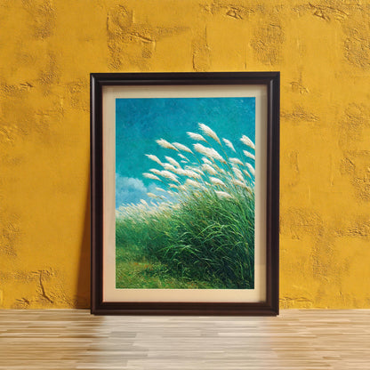 Wood-framed art print of a vibrant, textured painting showing white pampas grass (or reeds) blowing in a field of green against a bright, teal-blue sky. The framed artwork is leaning on a light wood floor against a textured, bright yellow-gold wall.