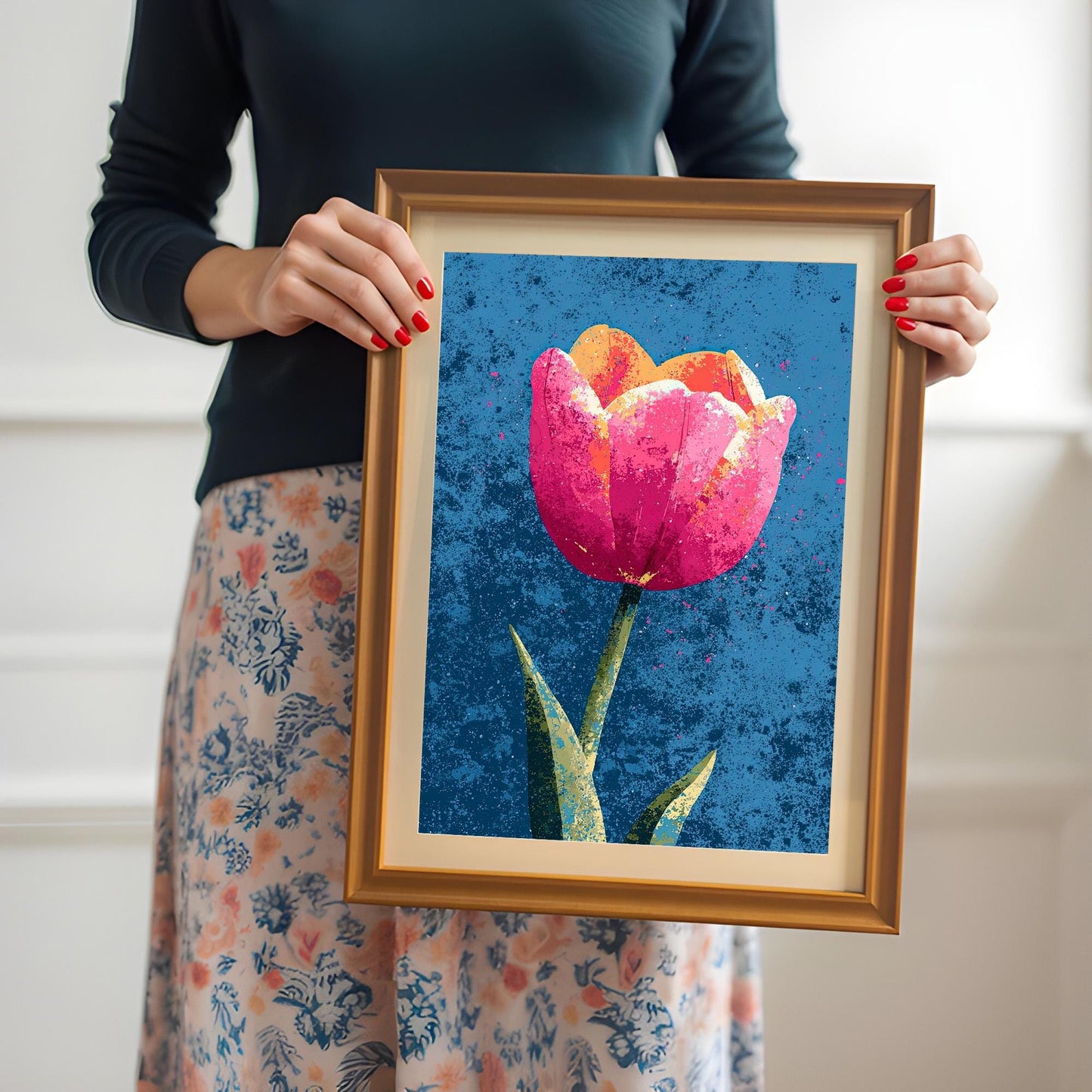 A woman in a dark shirt and floral skirt holding the framed tulip art print in an Orange Frame with both hands, showcasing the scale and clarity of the print.