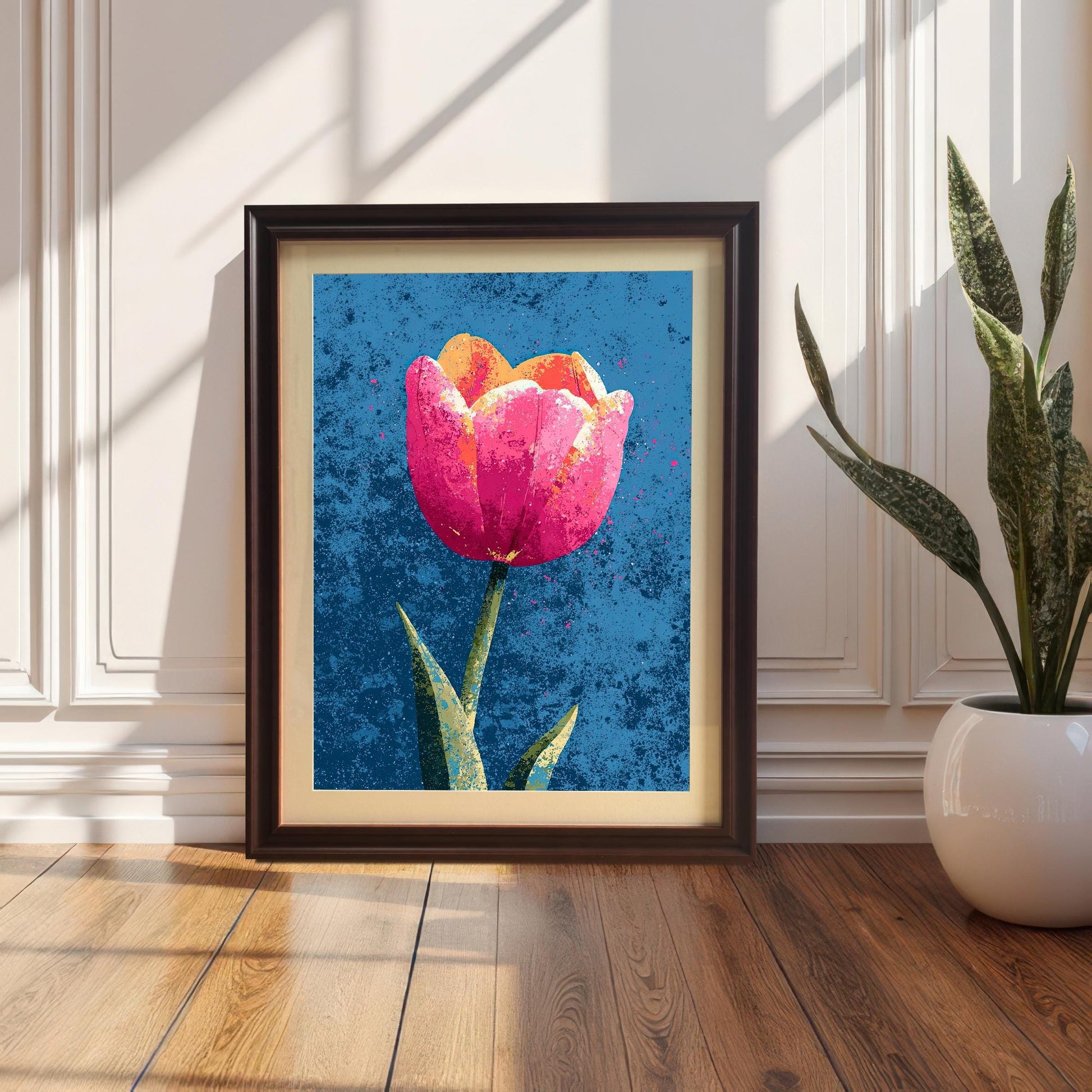 The vibrant tulip art print in a Black Wood Frame with a Mount (matting), leaning on a wood floor against a white wainscoted wall. A tall potted snake plant is visible on the right.